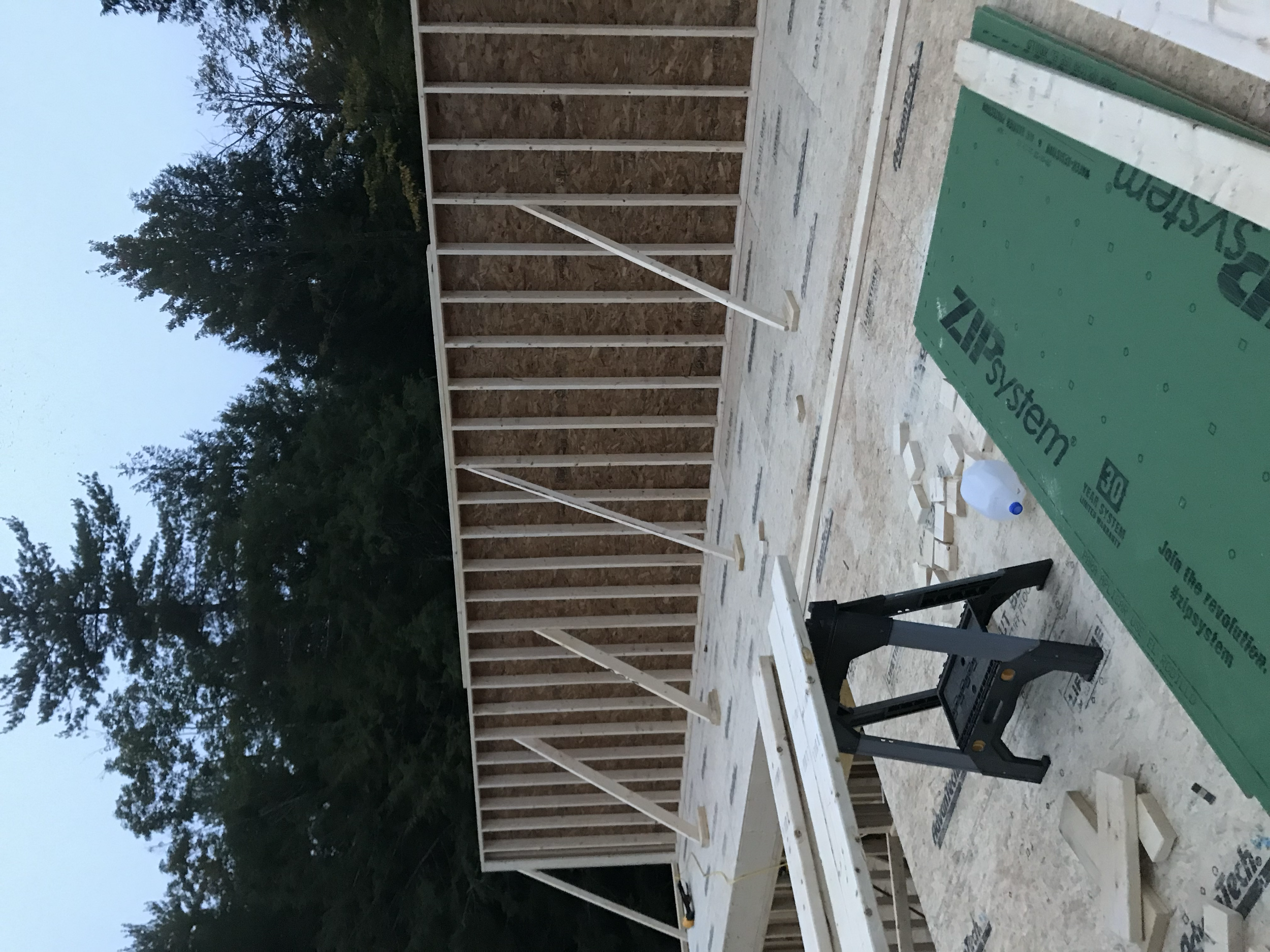 Construction site showing wooden framing for a building with trees in the background, construction materials on the floor, and a stepladder.