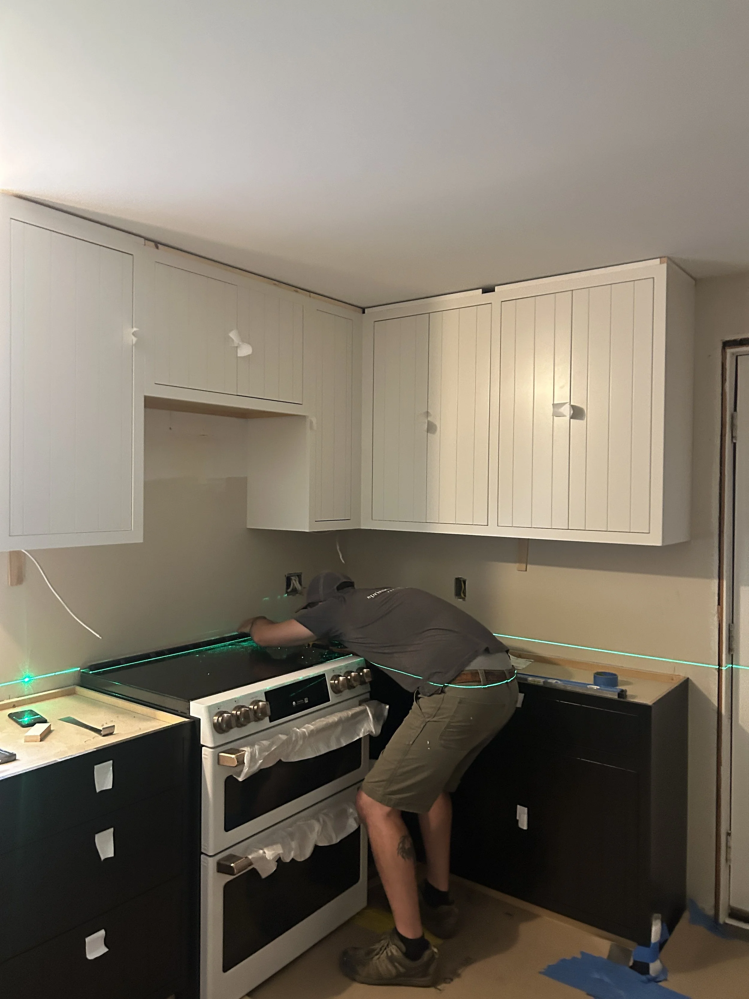 A person installing kitchen cabinets above a stove in a renovation project.