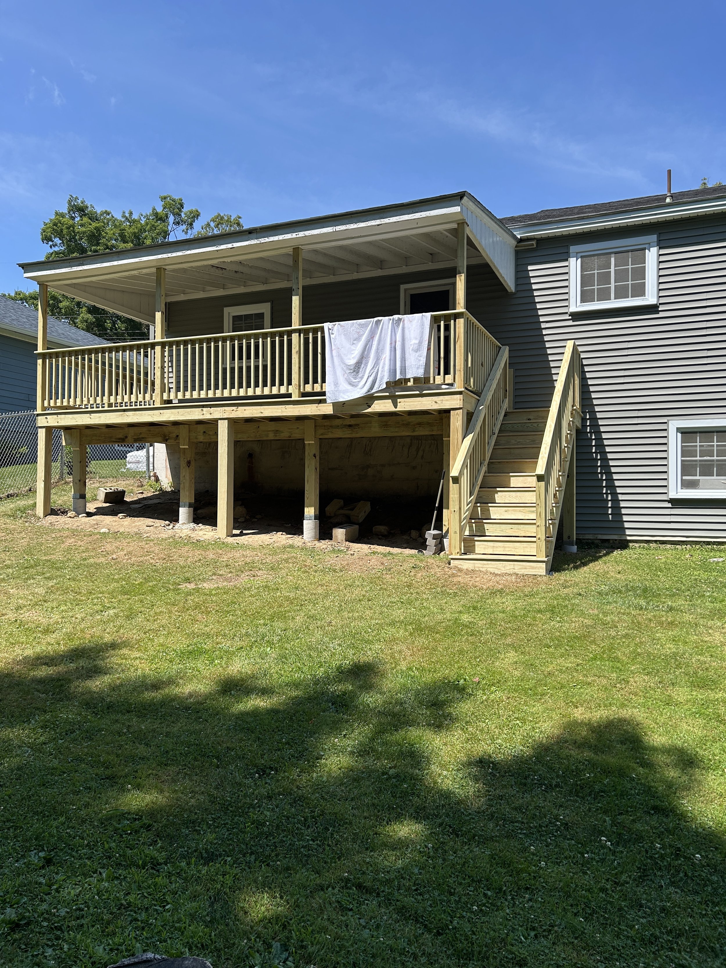 Backyard with newly built wooden deck and stairs, and a house with gray siding and white trim, under a blue sky.