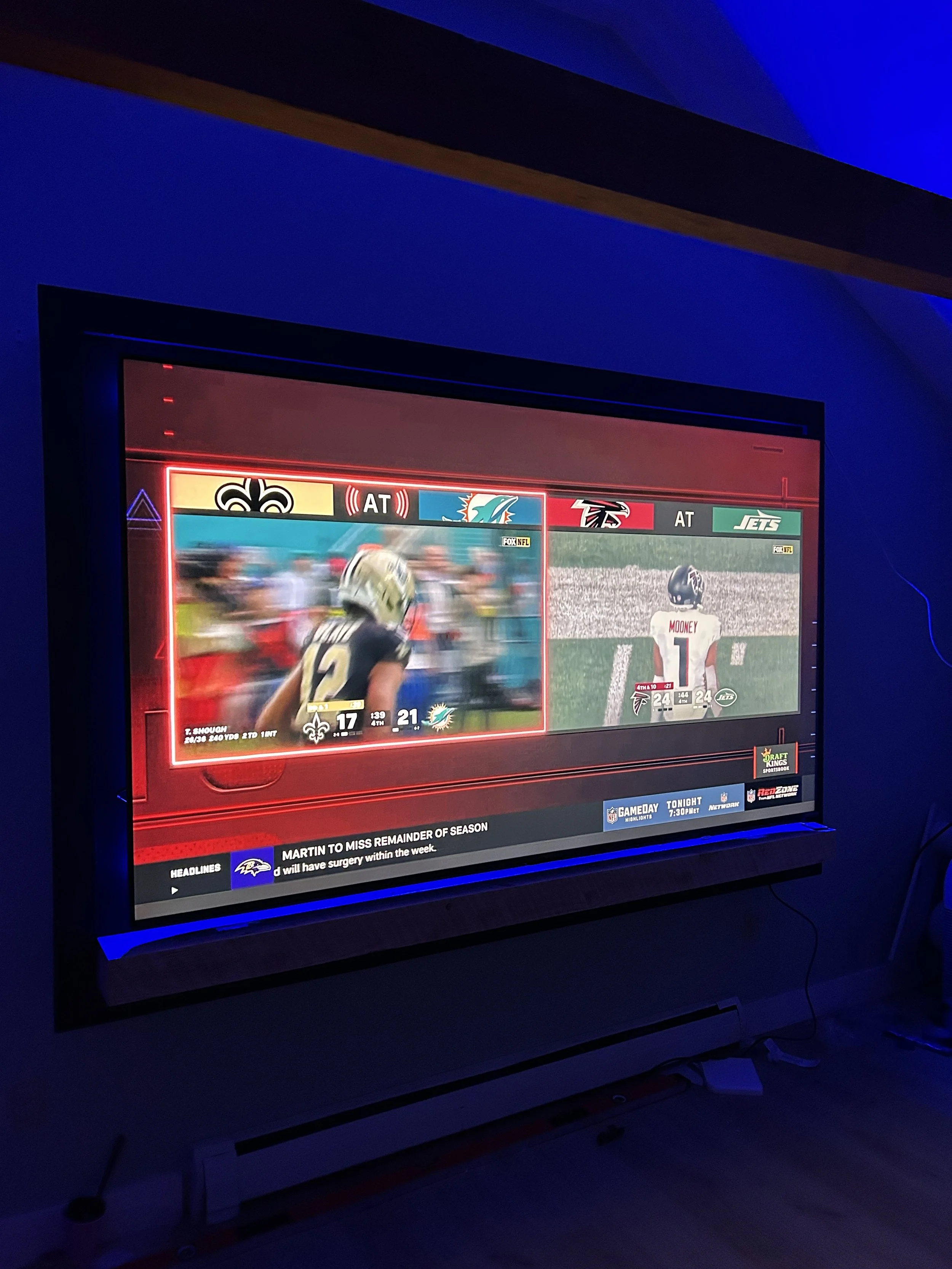 A television screen showing a split-screen of two NFL football games in a dark room with blue lighting.
