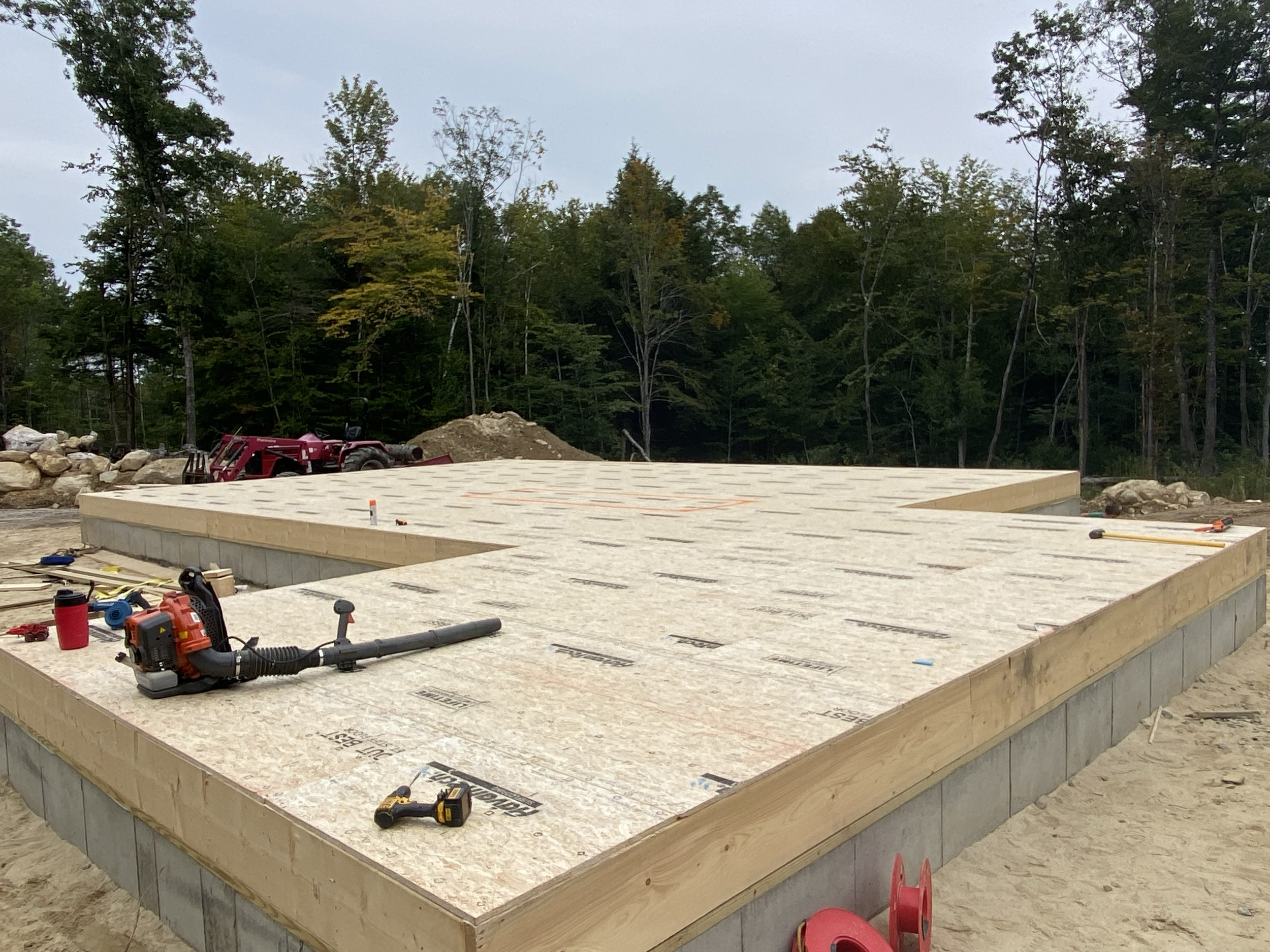 Construction site with wooden foundation with tools and equipment, surrounded by rocks and trees in the background.