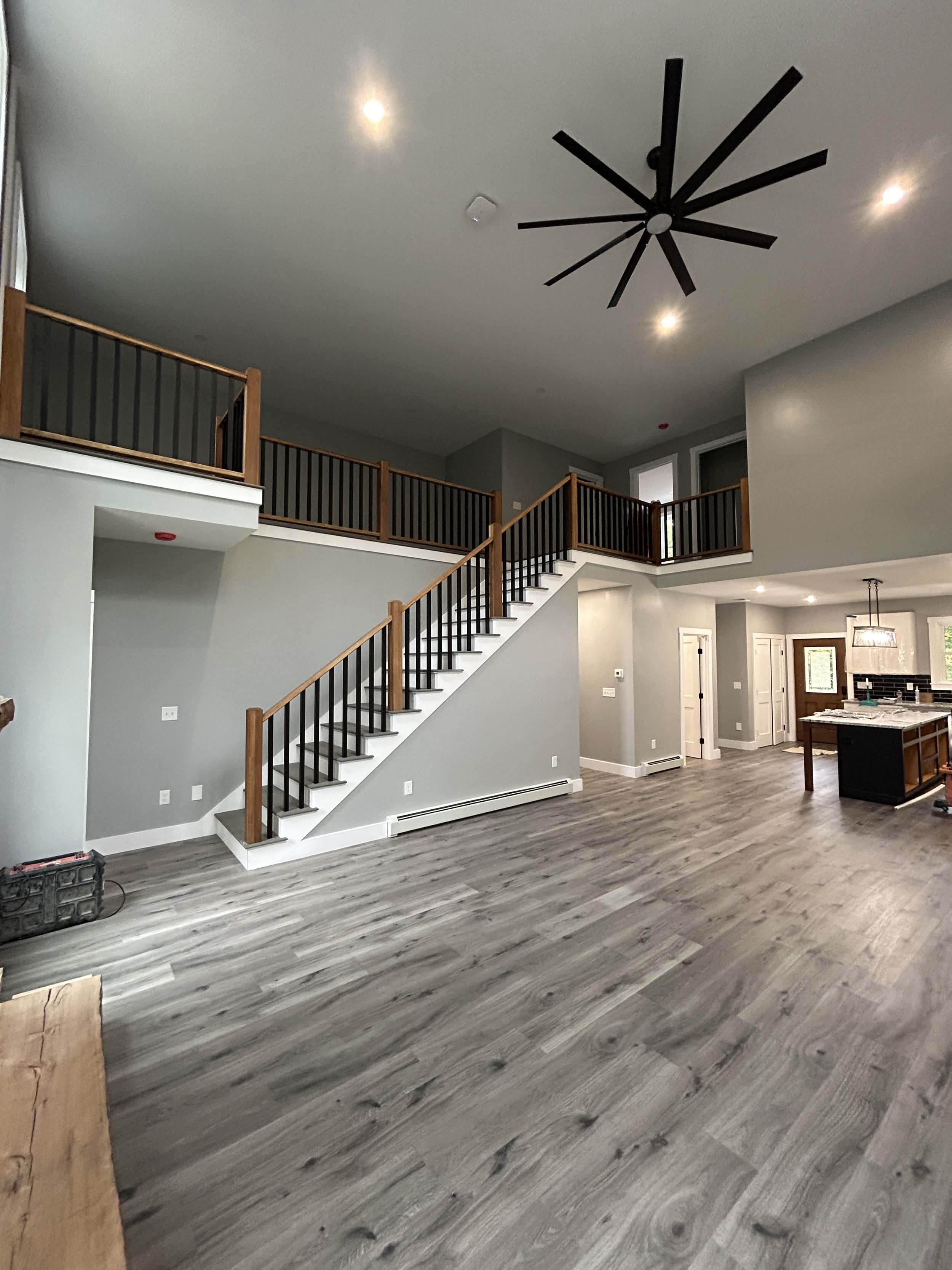 Interior of a modern house with a staircase, railing, and open living space featuring wood flooring and ceiling lighting.