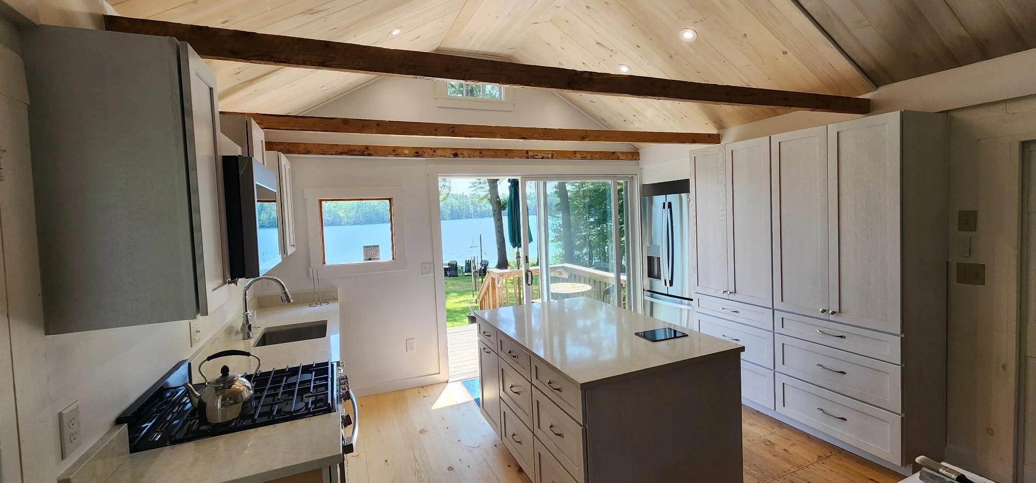 Kitchen with white cabinets, a central island, stainless steel refrigerator, and a view of a lake outside through glass doors and a window.