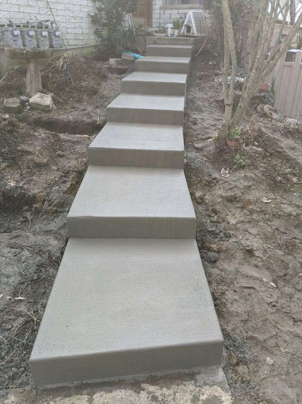 Concrete steps leading up a backyard with dirt and a few small trees on varying sides.