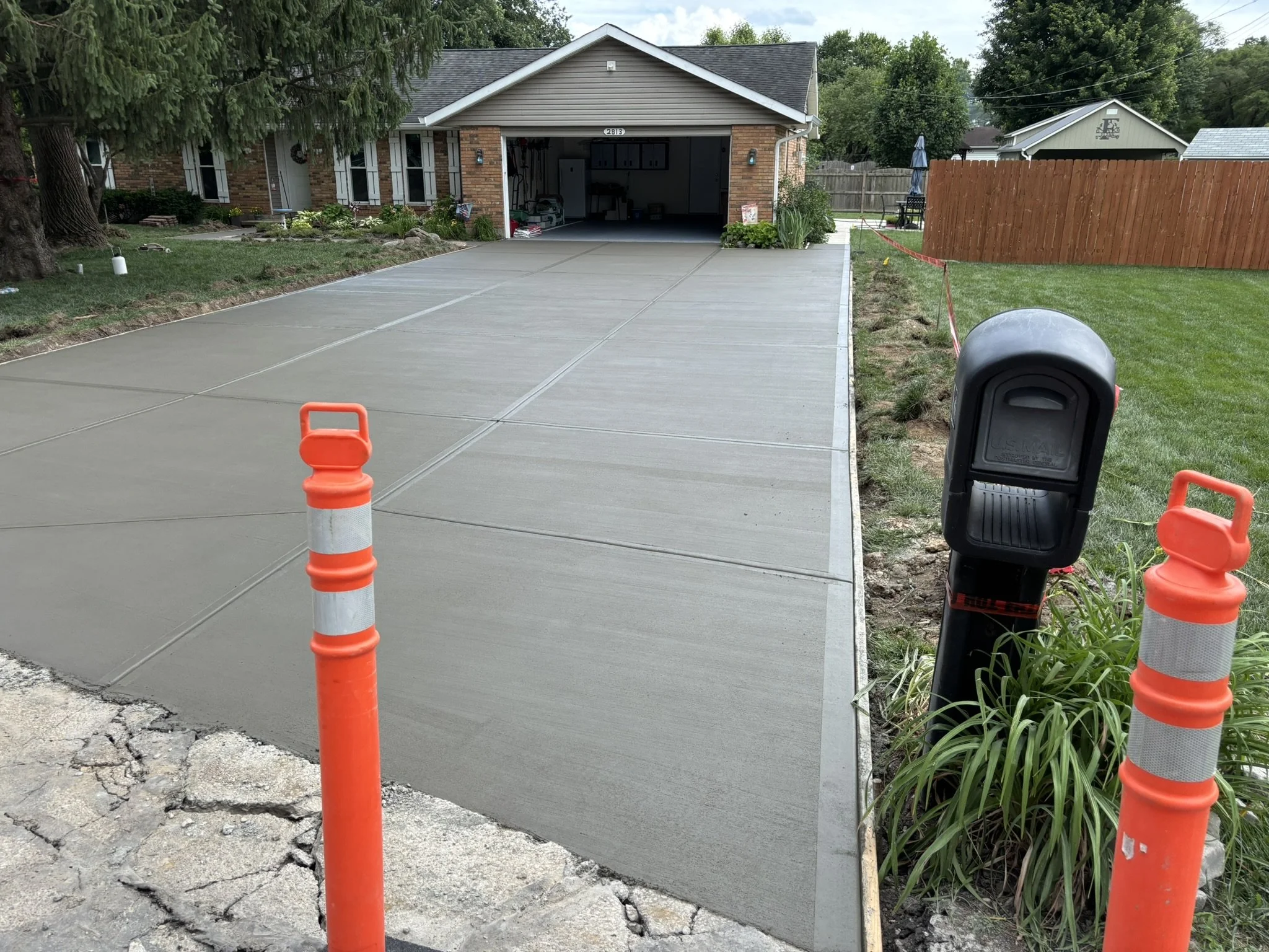 Newly poured concrete driveway in front of a garage with some construction safety cones and barriers in place during a sunny day.
