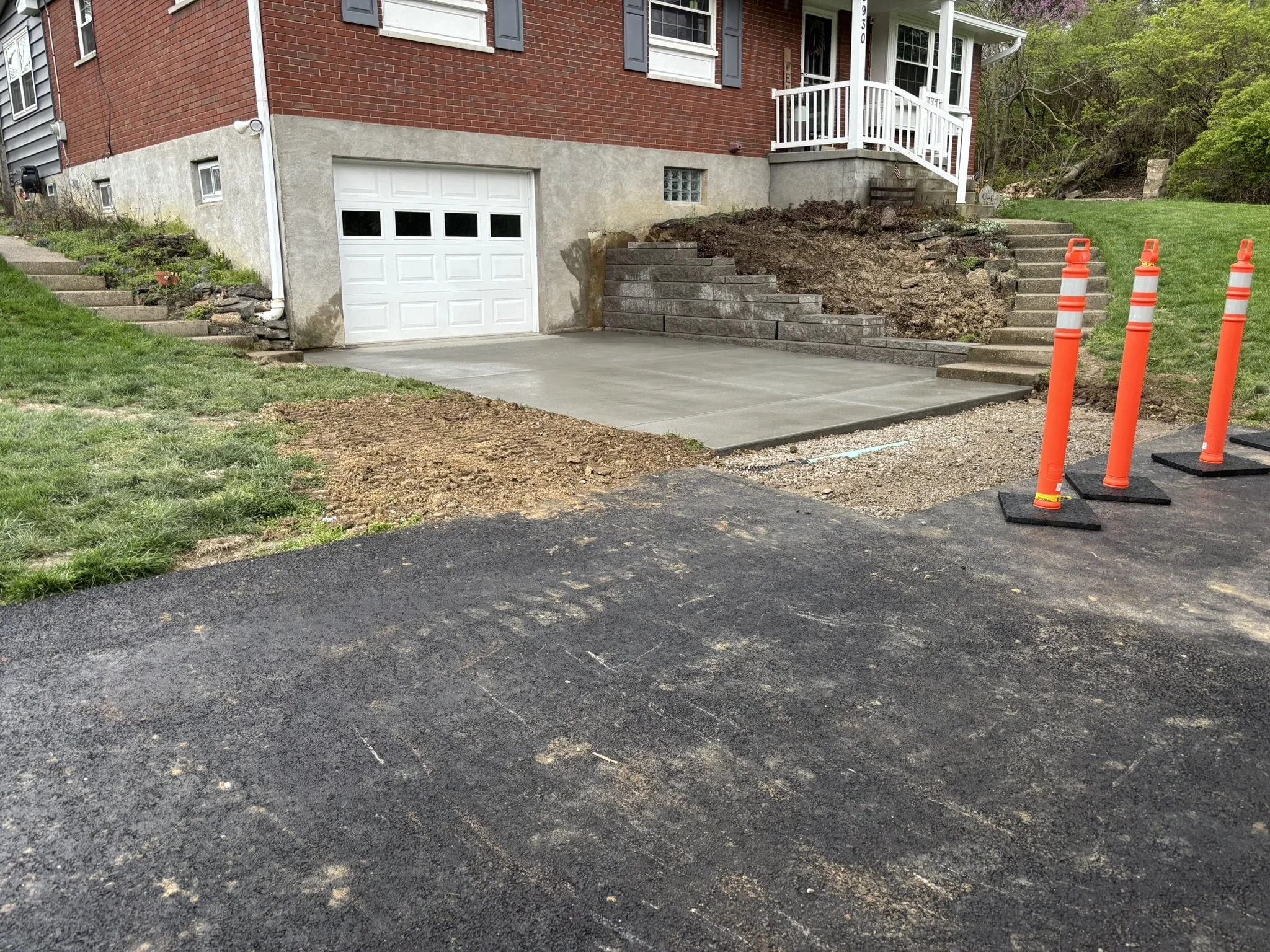Front yard of a house with a garage, concrete driveway, stairs, and orange safety cones, showing ongoing landscaping or construction work.
