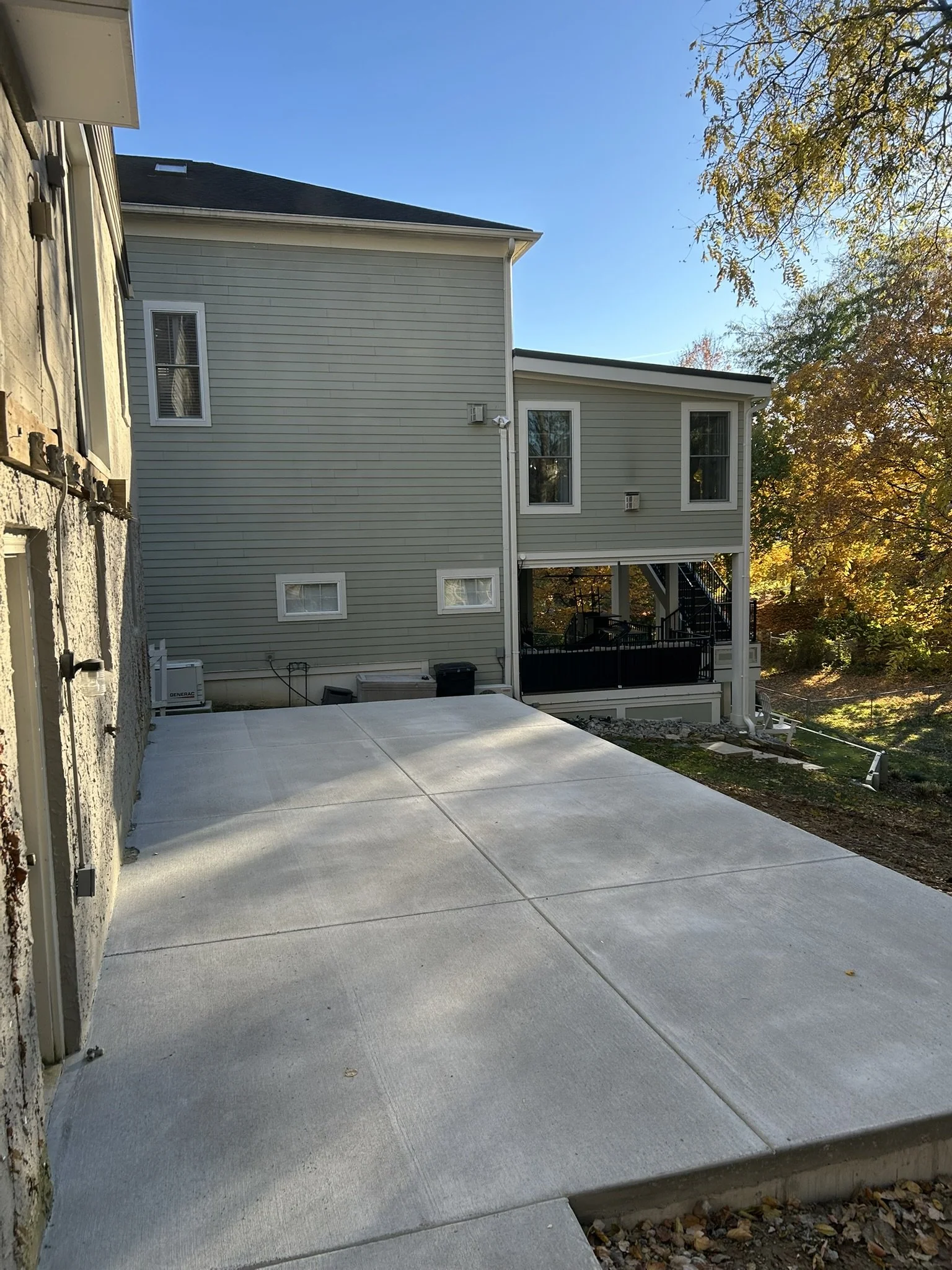 A concrete patio in a backyard with a blue house in the background surrounded by trees with fall foliage.