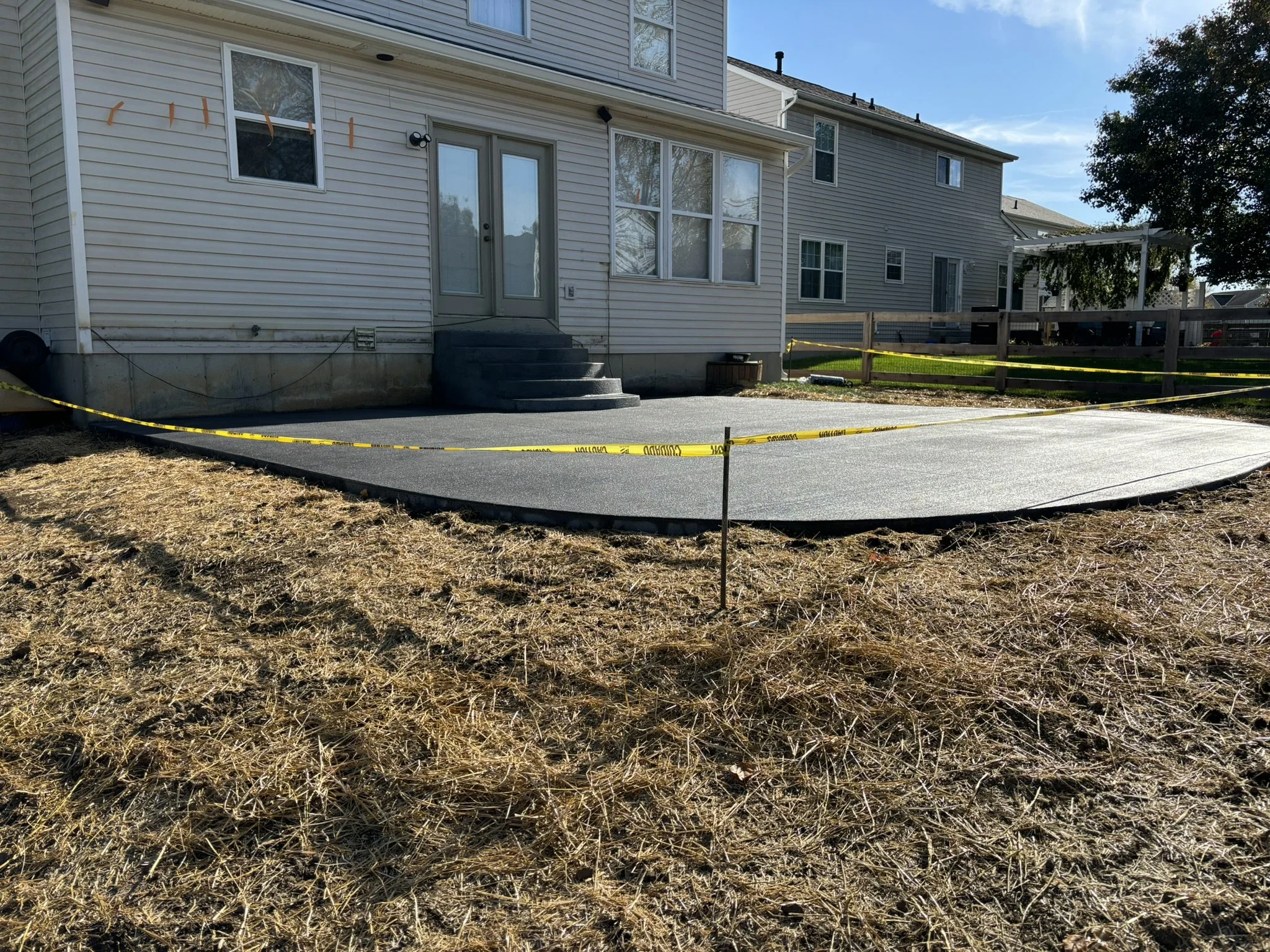 Backyard with a concrete patio, steps, a house with a porch, and a yellow caution tape surrounding the area.