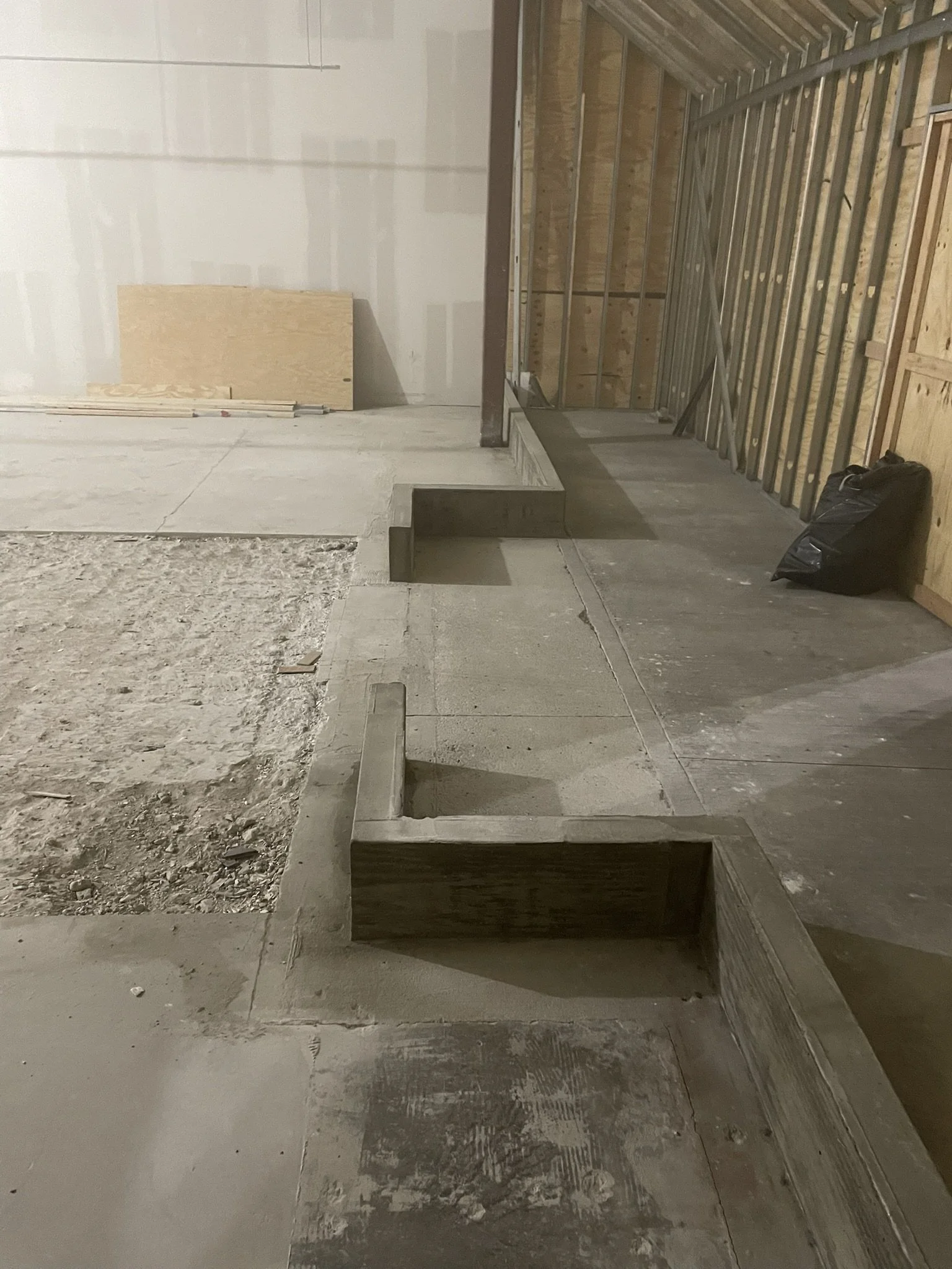 Construction site with unfinished flooring and walls, wooden and metal framing, and a black bag on the floor.