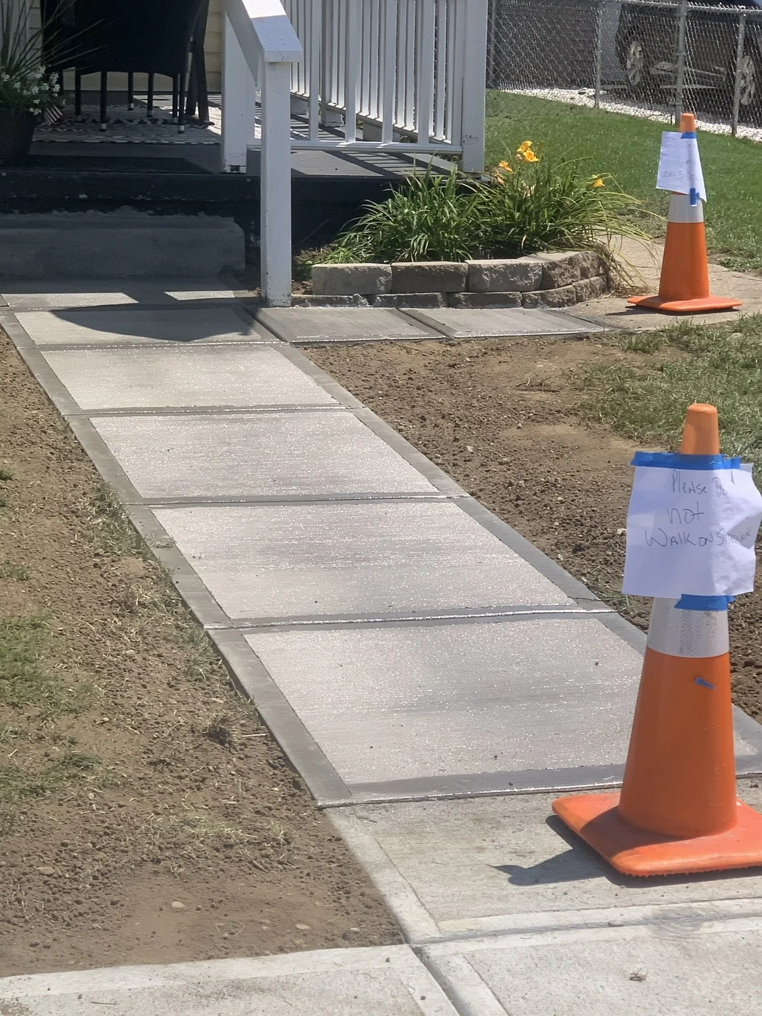 Sidewalk under construction with orange traffic cone and note that says 'Please do not walk on'.