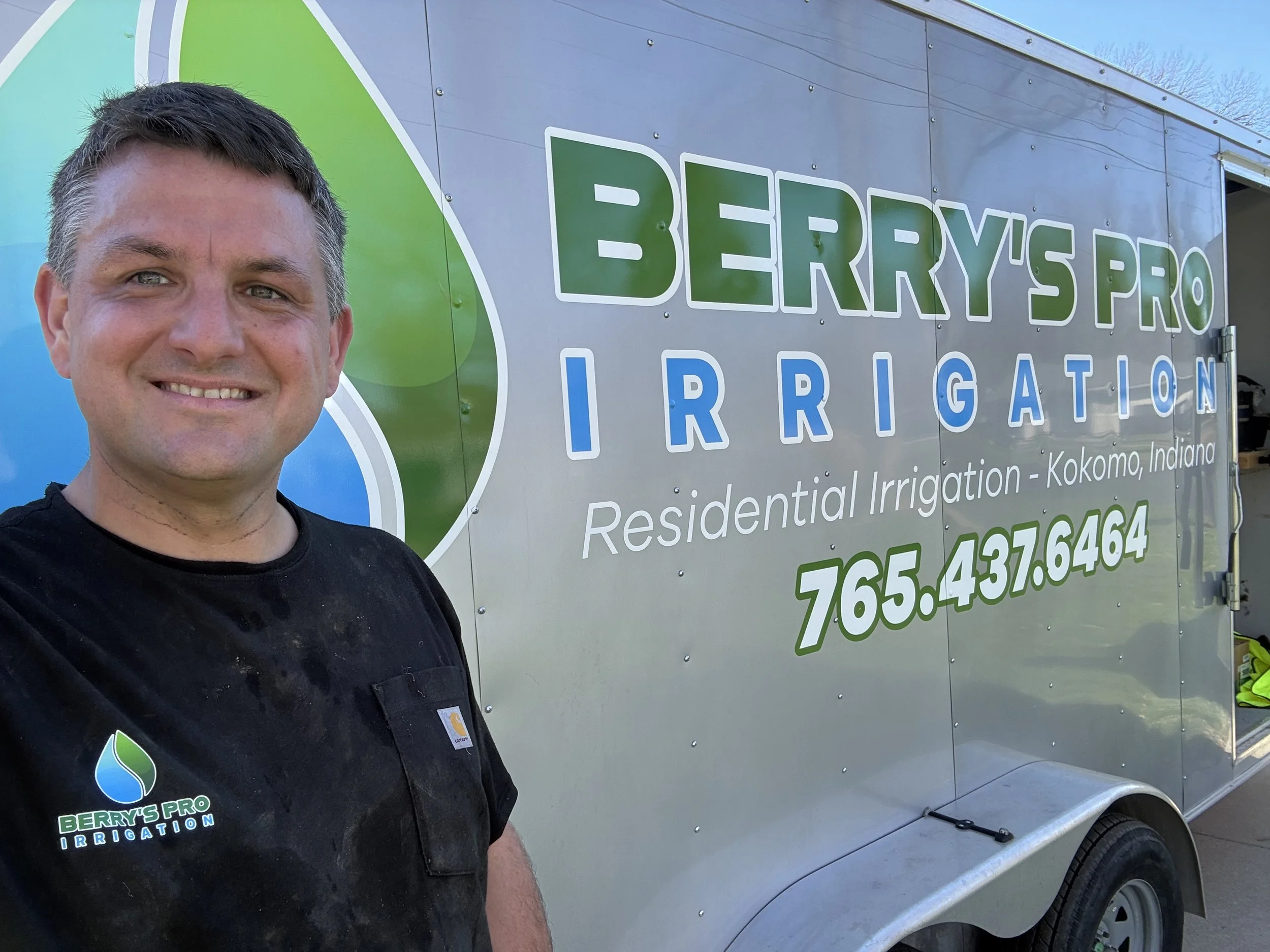 A man taking a selfie in front of a silver service truck with green and blue branding for Berry's Pro Irrigation. The truck displays the company's name, phone number, and services offered.