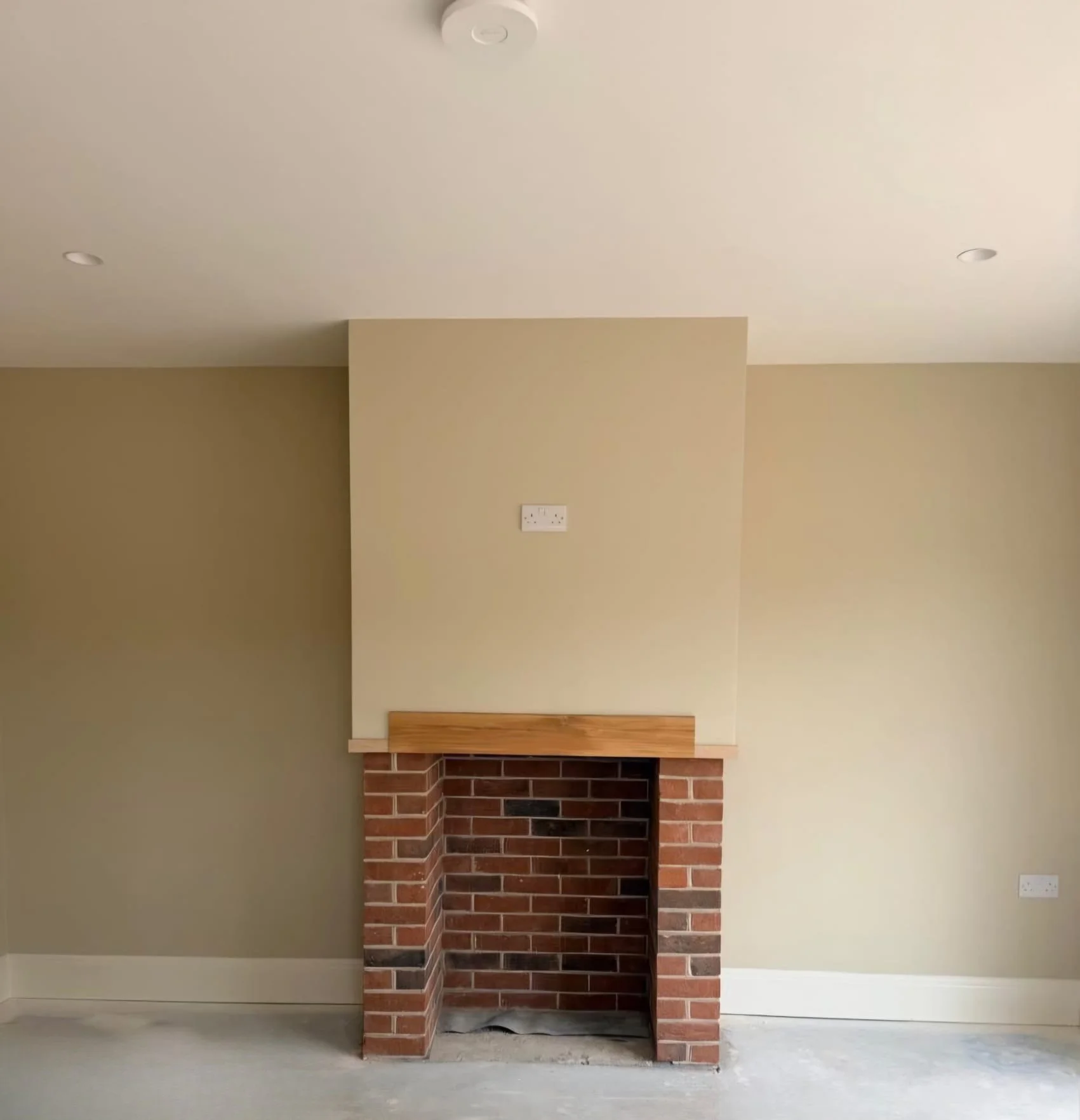 Empty brick fireplace with wooden mantel in a room with beige walls, electrical outlets, and a ceiling smoke detector.