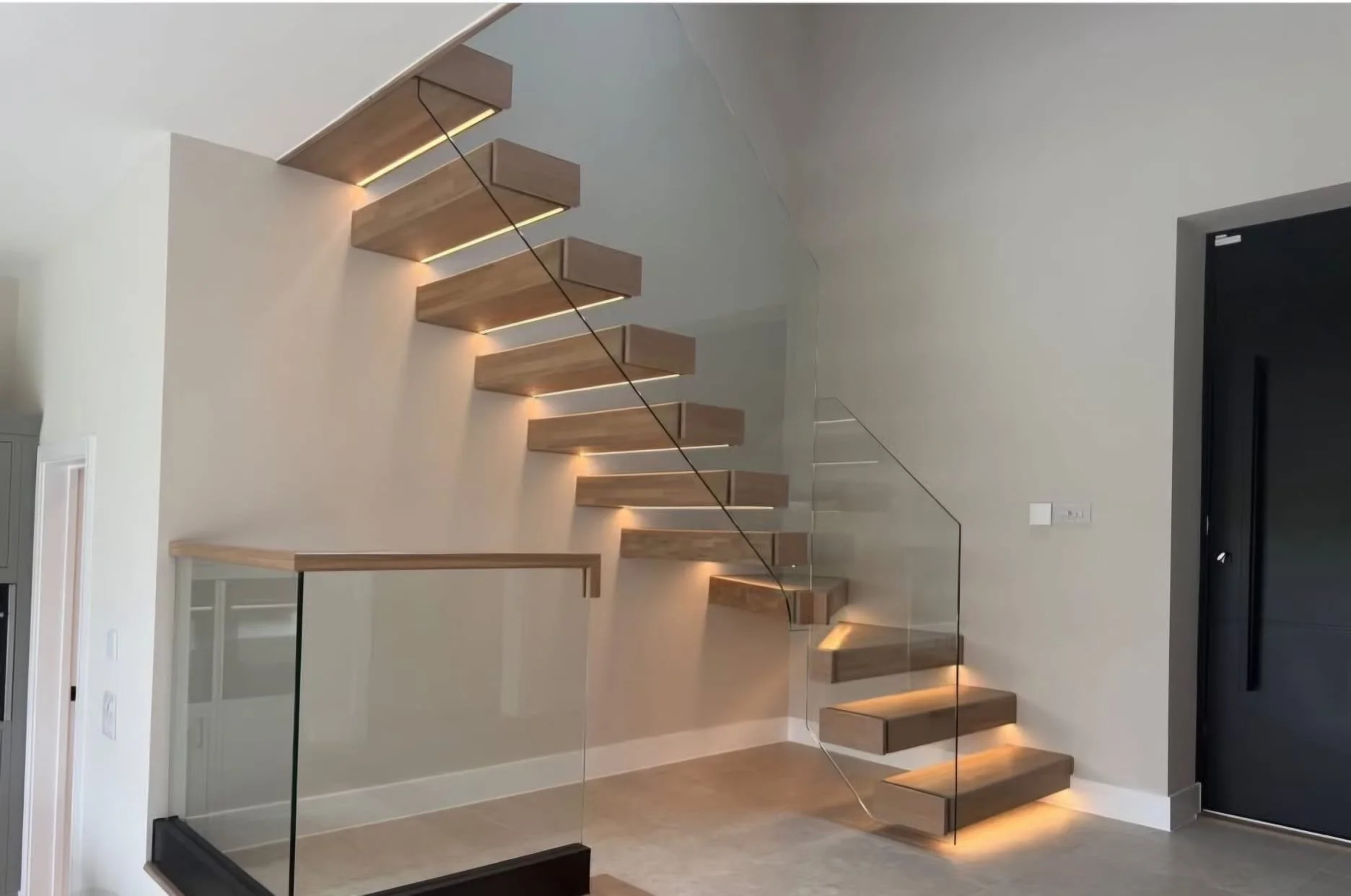 Modern floating wooden staircase with glass railing and integrated lighting in a minimalist interior space.