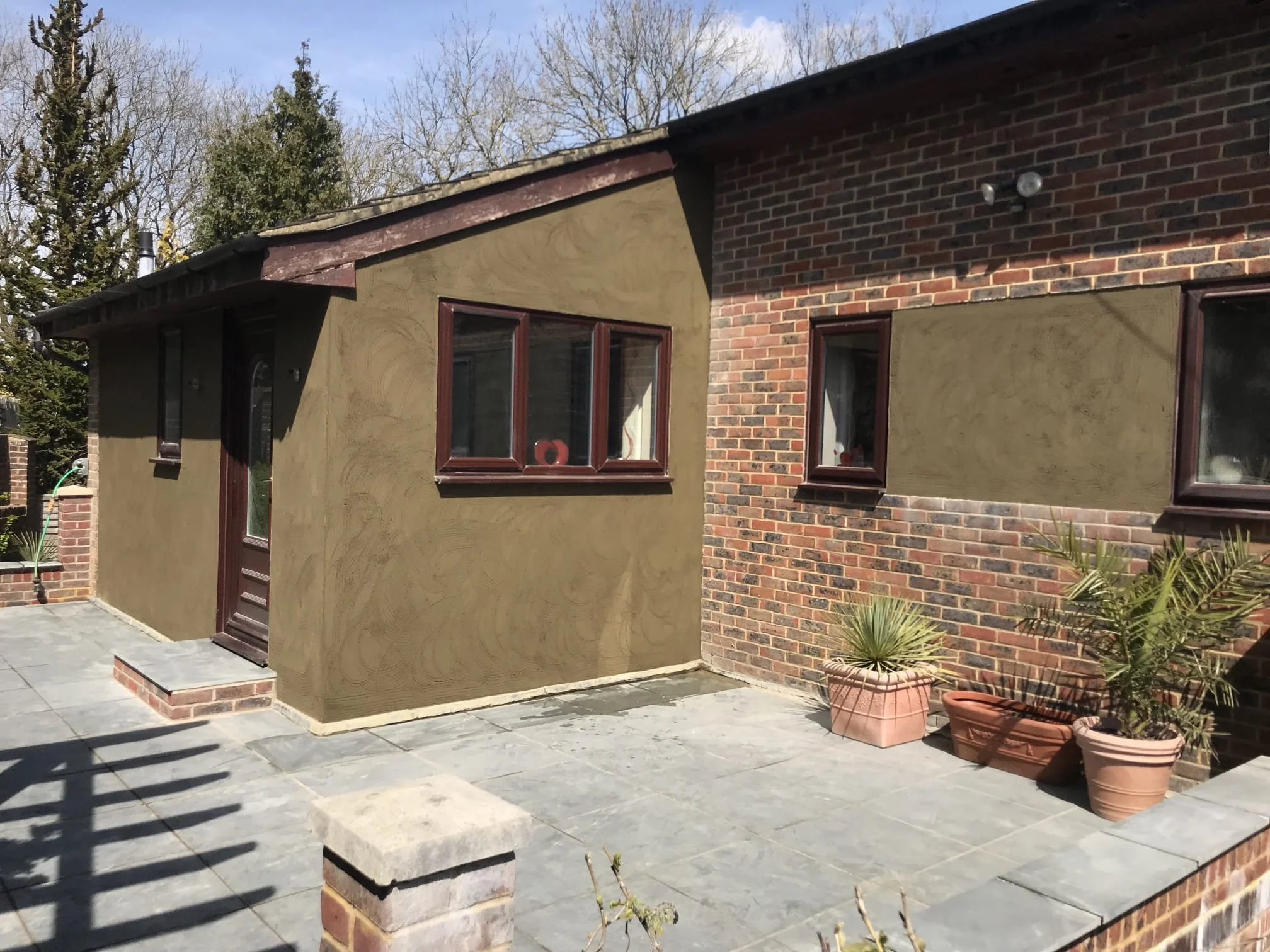 Backyard patio with large stone tiles, potted plants, and a modern house featuring a mix of brick and stucco exterior walls.