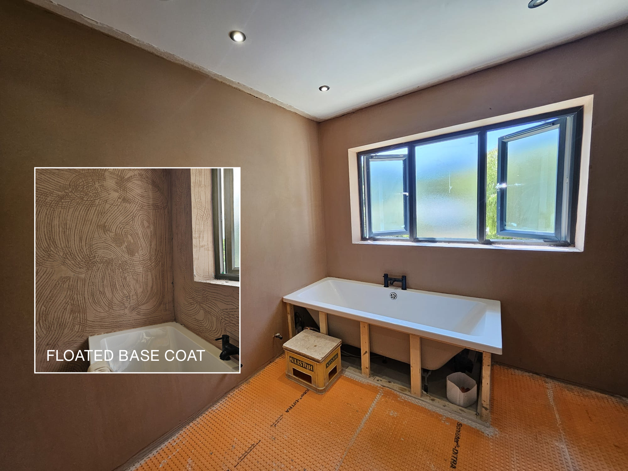 In a bathroom under renovation, a bathtub is installed below a window with open windows. The wall behind the bathtub is prepared for tiling with a floating base coat, showcasing a textured pattern. The floor is covered with orange construction mesh for underlayment.