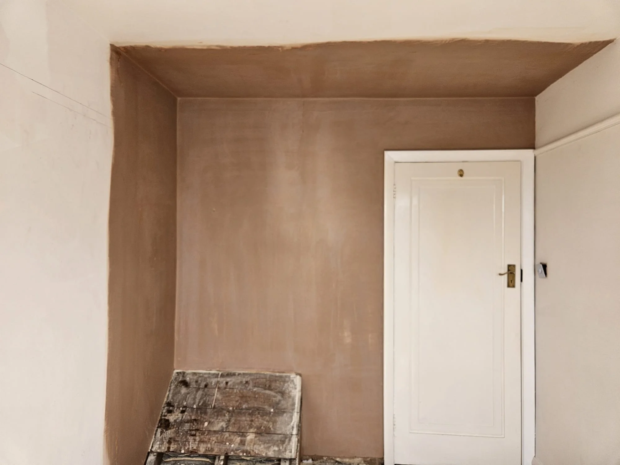 Empty room with brown painted walls, a white door with a gold handle, and a small radiator on the floor.