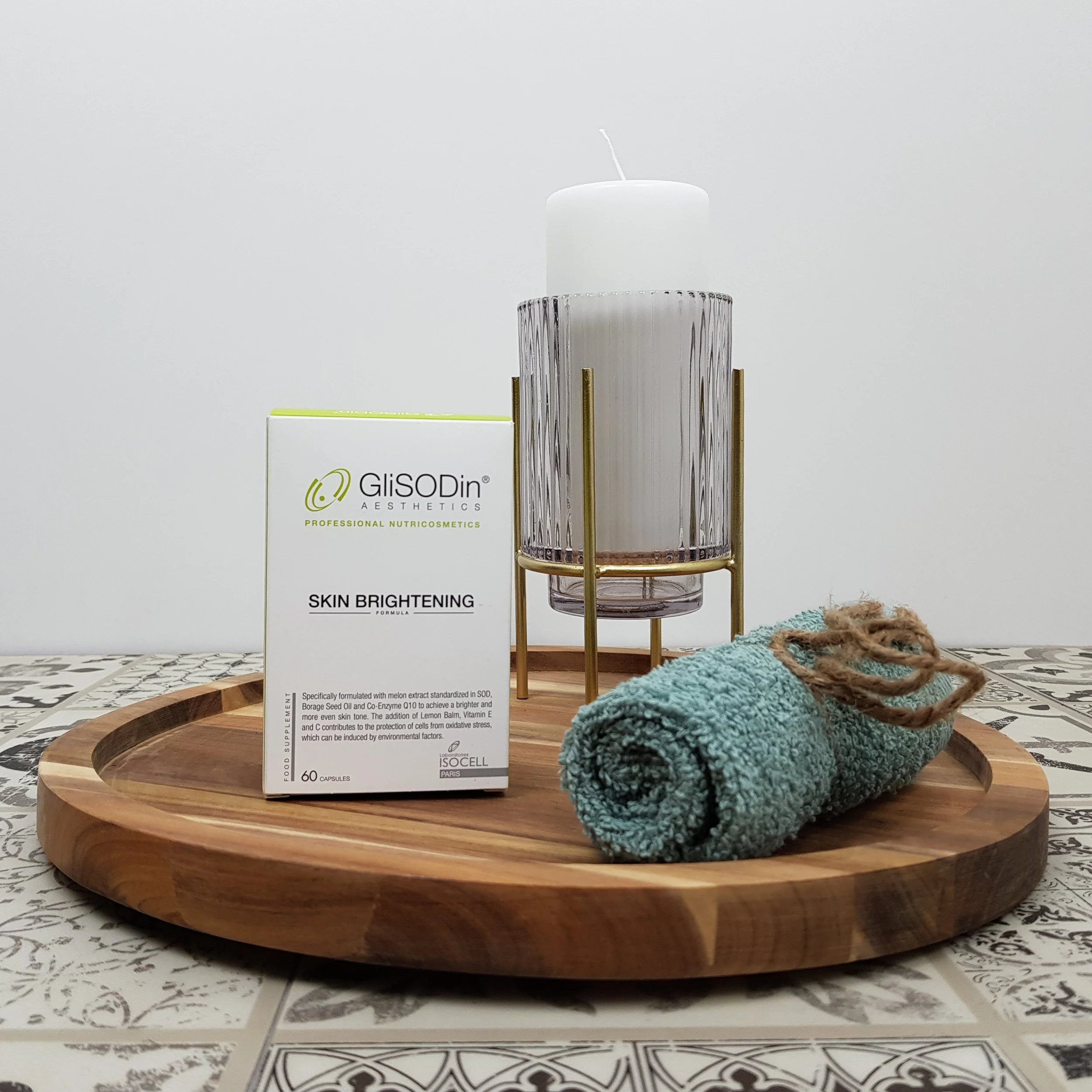 A skincare product box labeled 'GisODin Aesthetics Skin Brightening Formula' placed on a wooden tray with a textured ceramic cup and a cozy sock nearby.