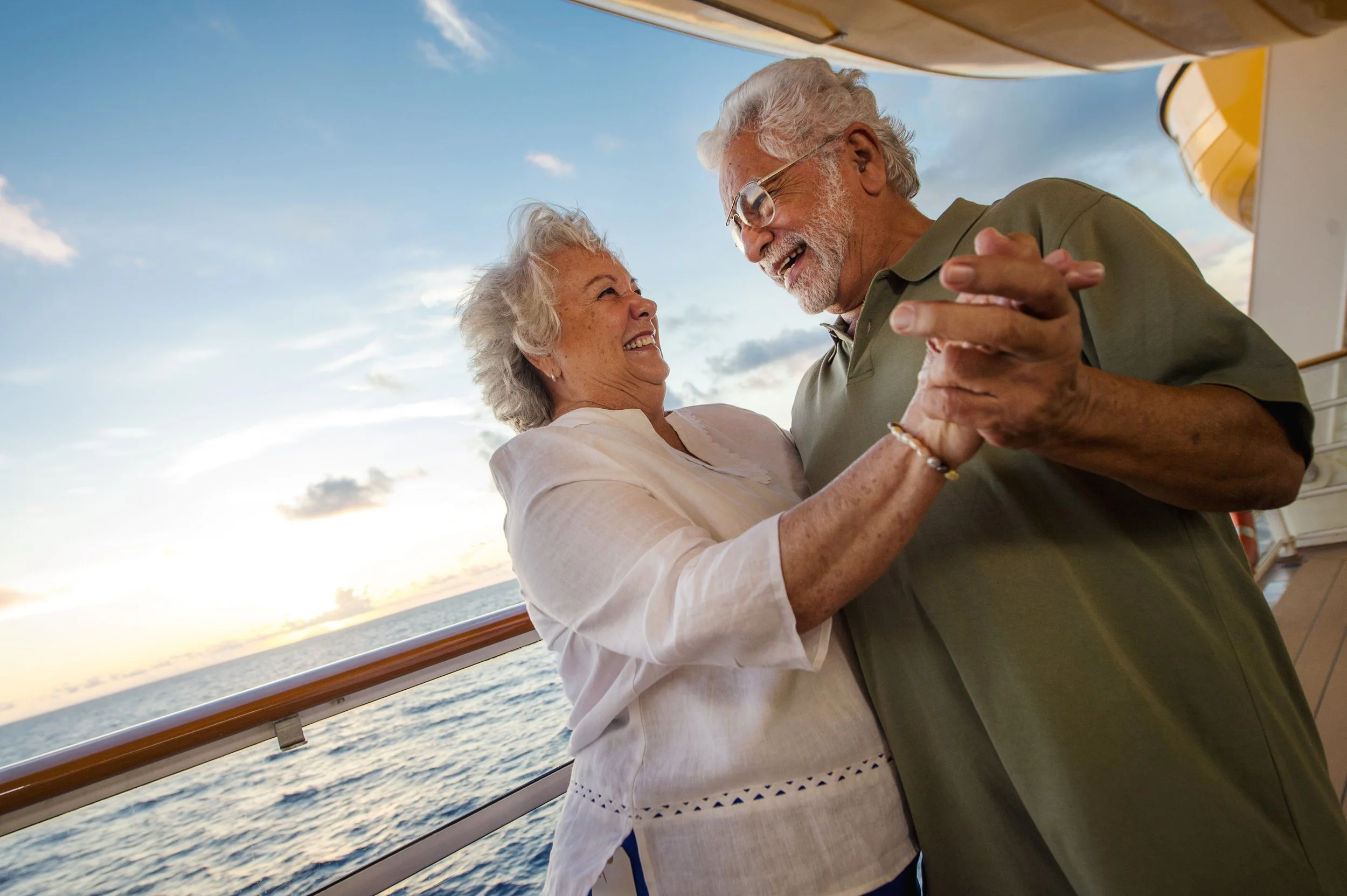 An elderly couple dancing on a boat during sunset, with the ocean in the background.