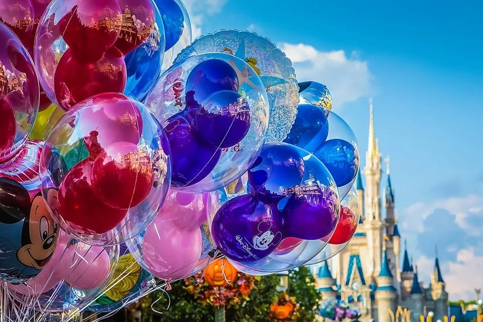 Colorful balloons, including some with Disney characters, at Disneyland with Sleeping Beauty Castle in the background.