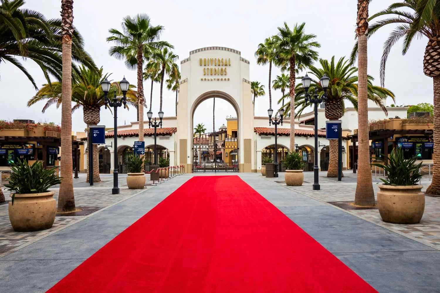 Entrance to Universal Studios Hollywood with a red carpet leading to the gates, surrounded by palm trees and decorative lamp posts.