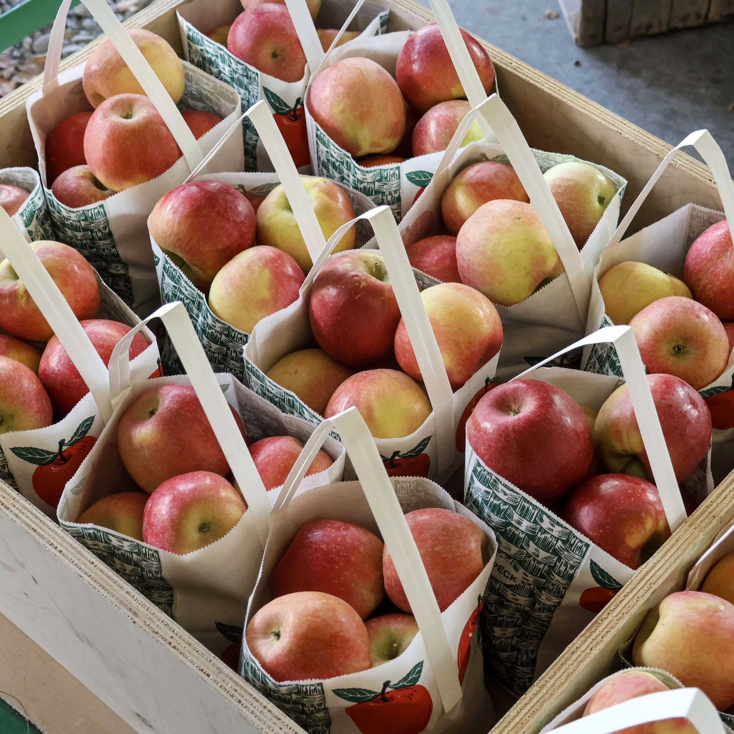 Multiple apples in paper bags inside a wooden crate at a market or store.