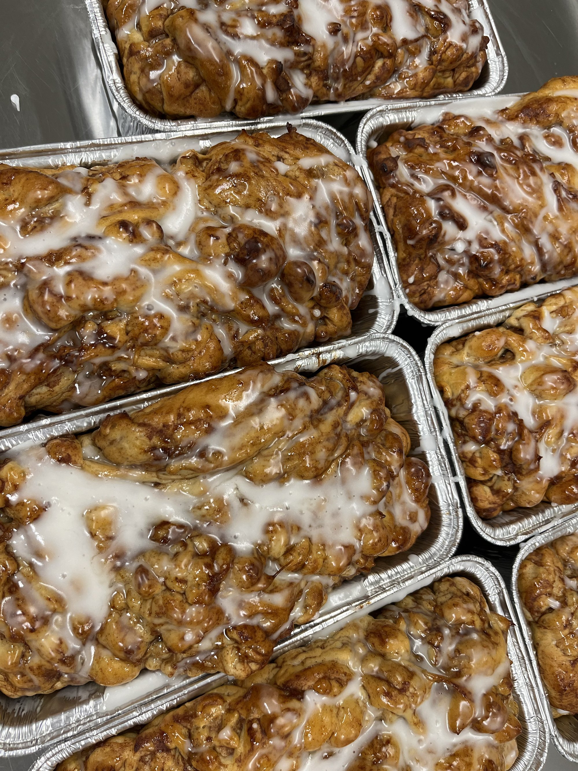 Multiple aluminum trays filled with baked loafs topped with a white icing glaze.