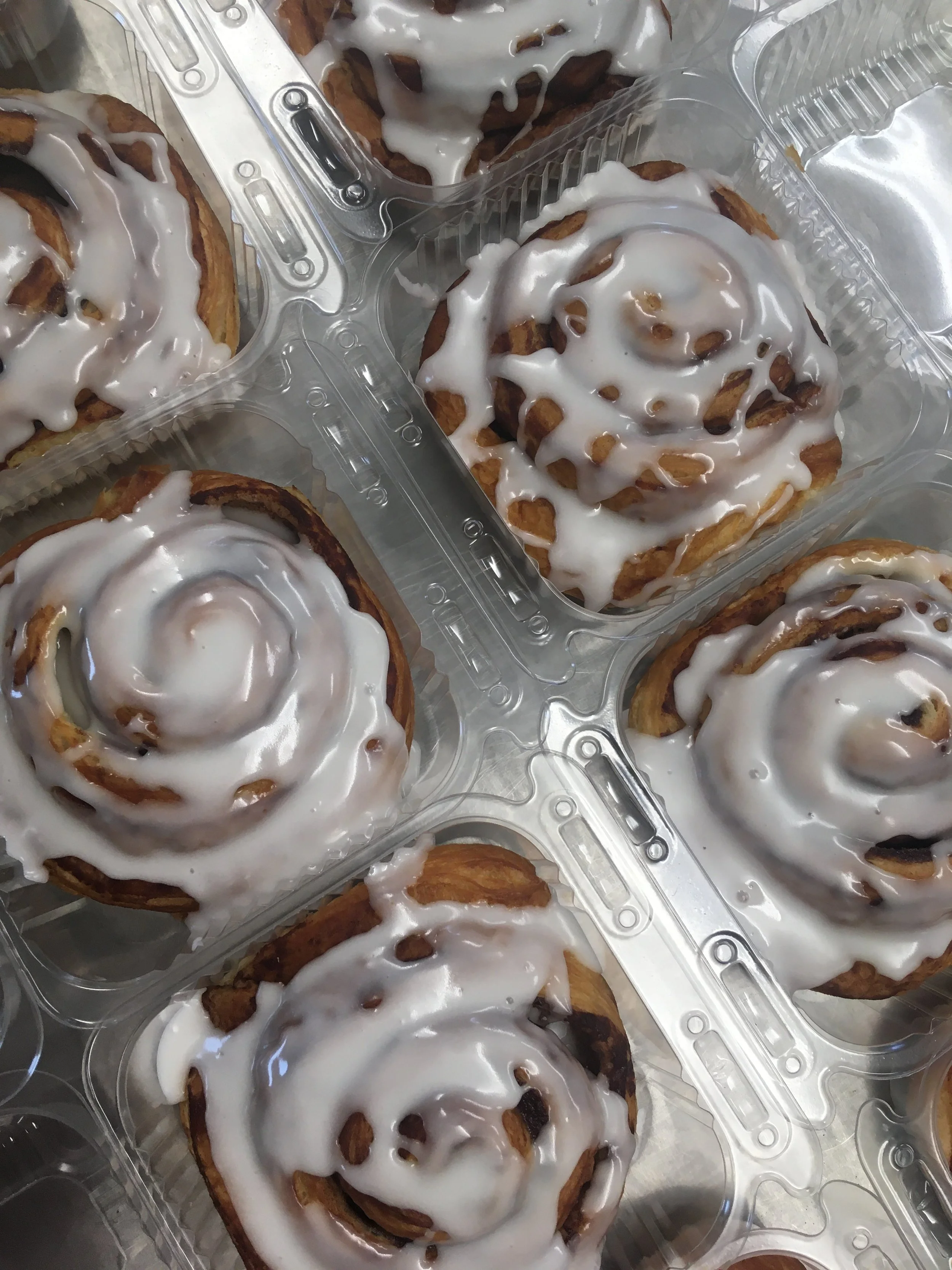 Homemade cinnamon rolls with white icing in food containers.