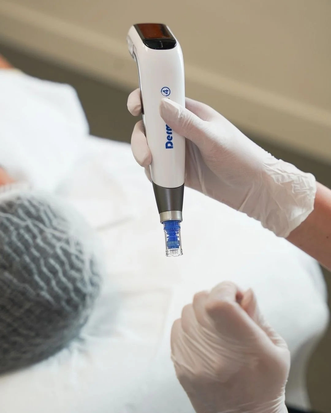 A healthcare professional wearing gloves holding a medical device, possibly a blood glucose monitor or similar instrument, over a patient's hand.