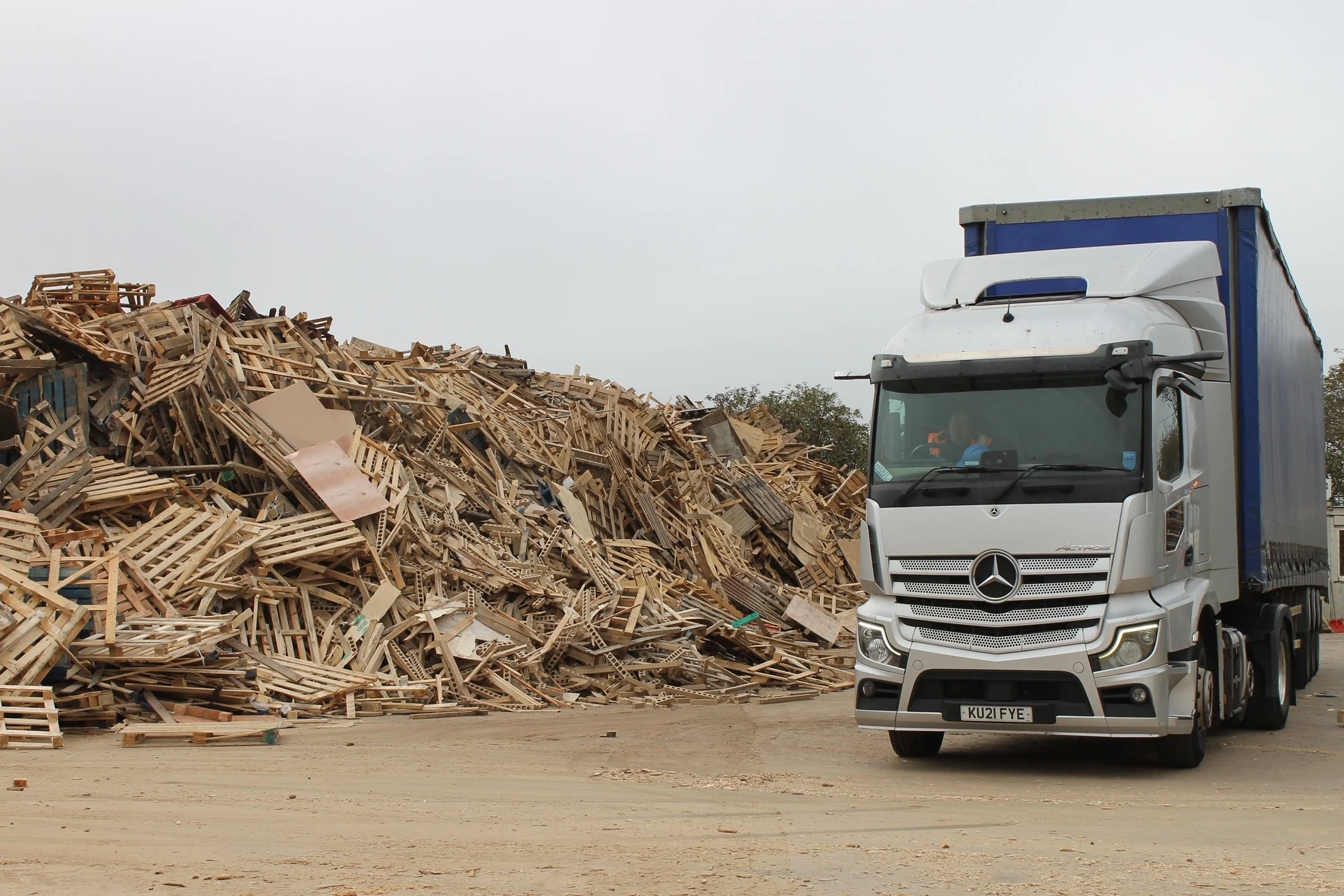 A Mercedes-Benz truck parked on a dirt surface beside a large pile of discarded wooden pallets and debris.