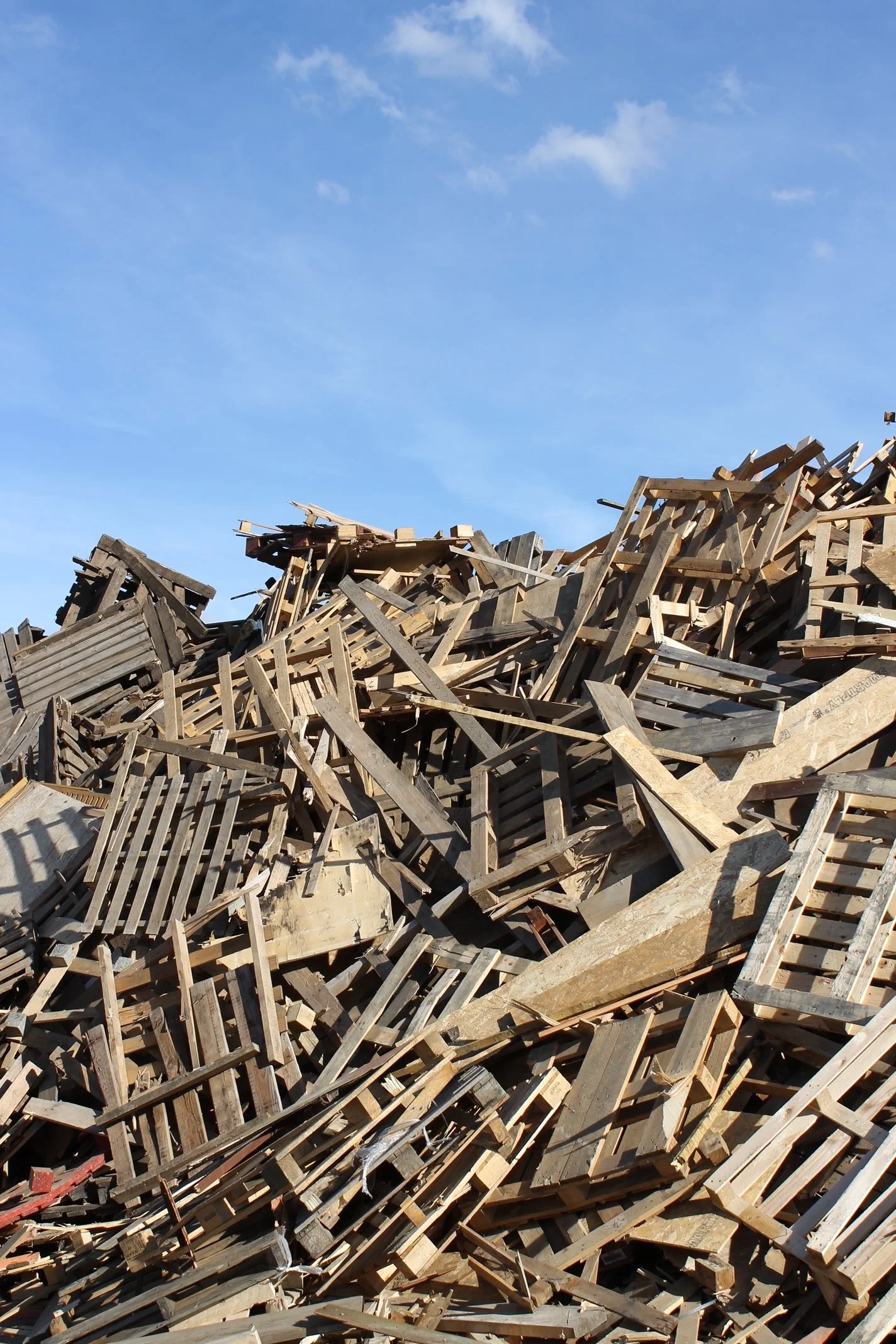 Pile of discarded wooden pallets and debris under a blue sky.
