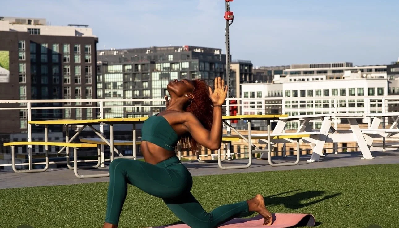 A woman practicing yoga outdoors on a rooftop with city buildings in the background.