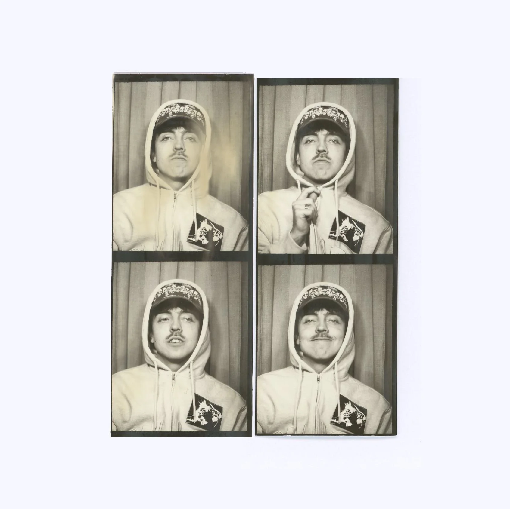 Four black and white portraits of a young man wearing a hoodie with a graphic patch, posing in front of a curtain background. The photos show different facial expressions and gestures.