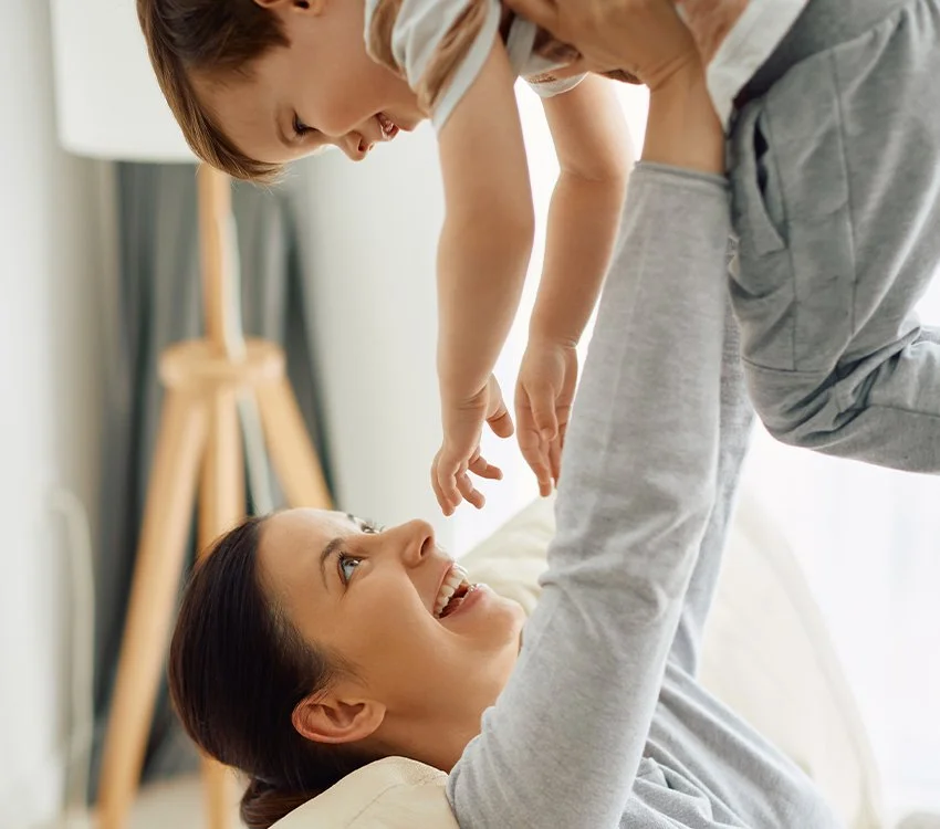 Une mère et son enfant jouent joyeusement sur un canapé dans un salon lumineux.