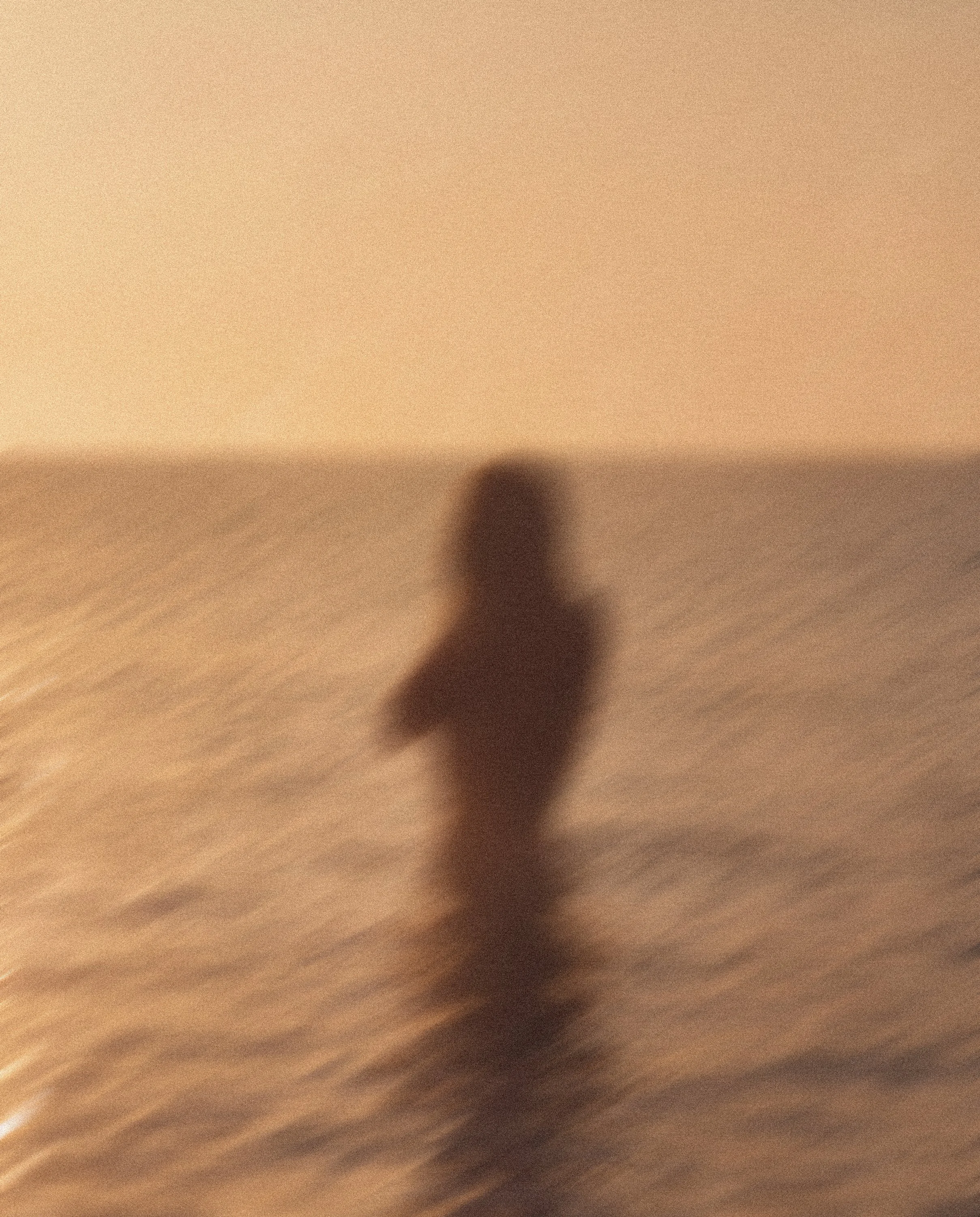 A person's finger is pointing towards a blurry, indistinct background with warm beige and brown tones.