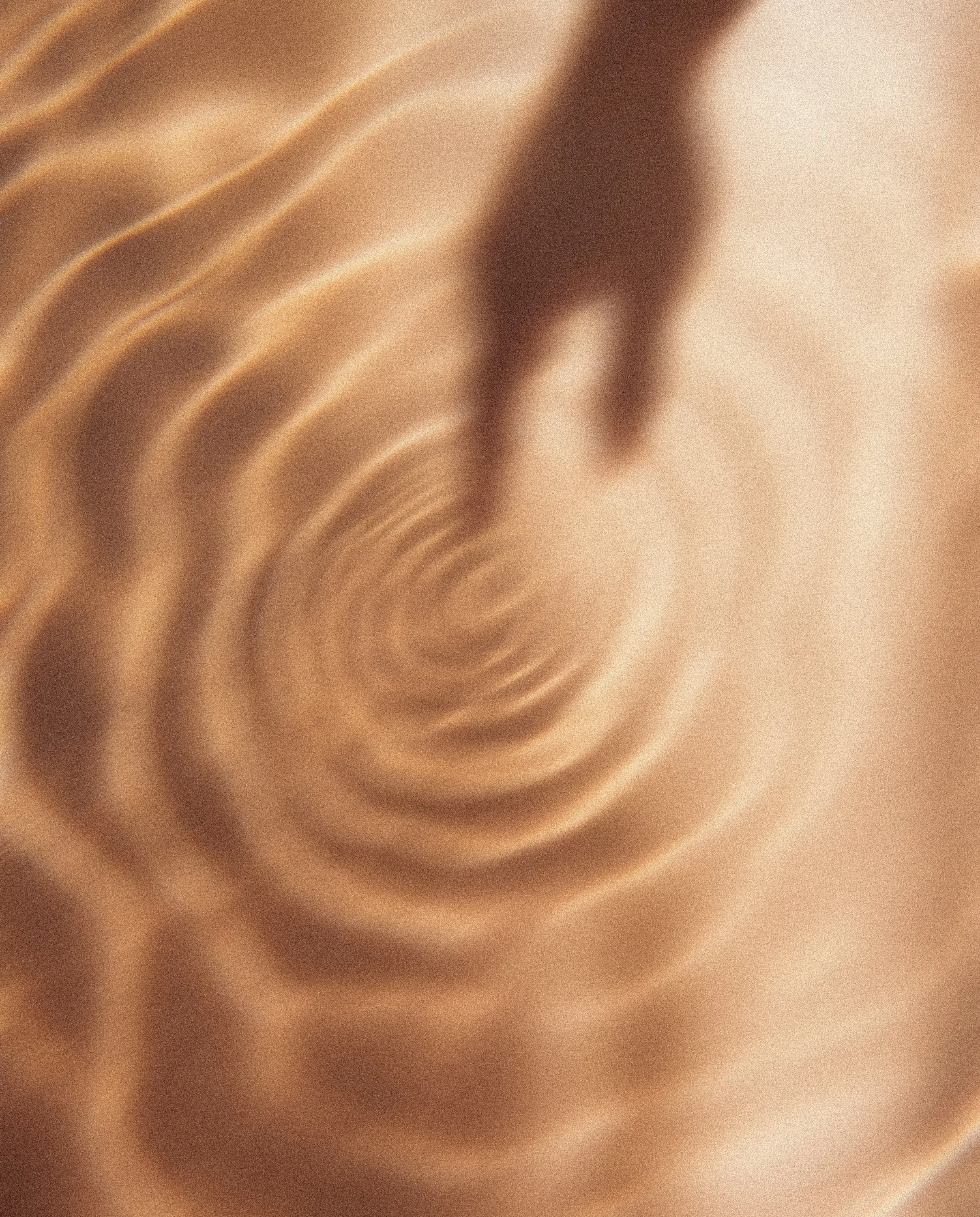 Close-up of a piece of smooth, twisted beige or light brown fabric with soft folds and ripples.