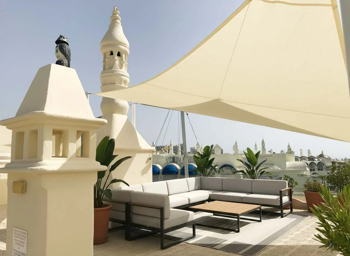 Terraza junto a la marina en Fuengirola con velas de sombra, sillones y plantas.