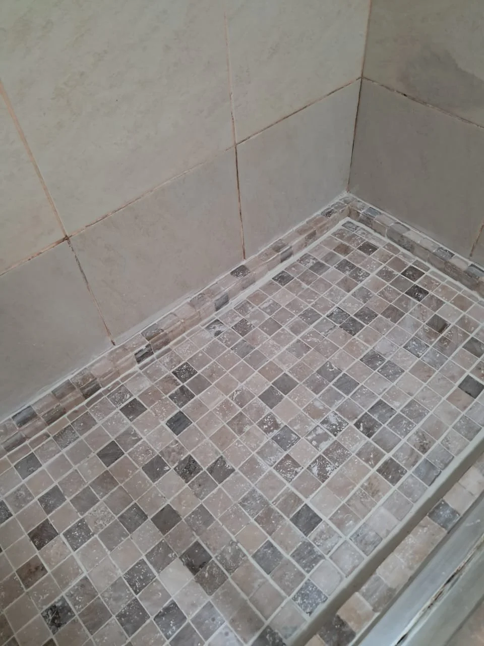 A tiled shower floor with small square mosaic tiles in shades of beige, brown, and gray, with a built-in drain.