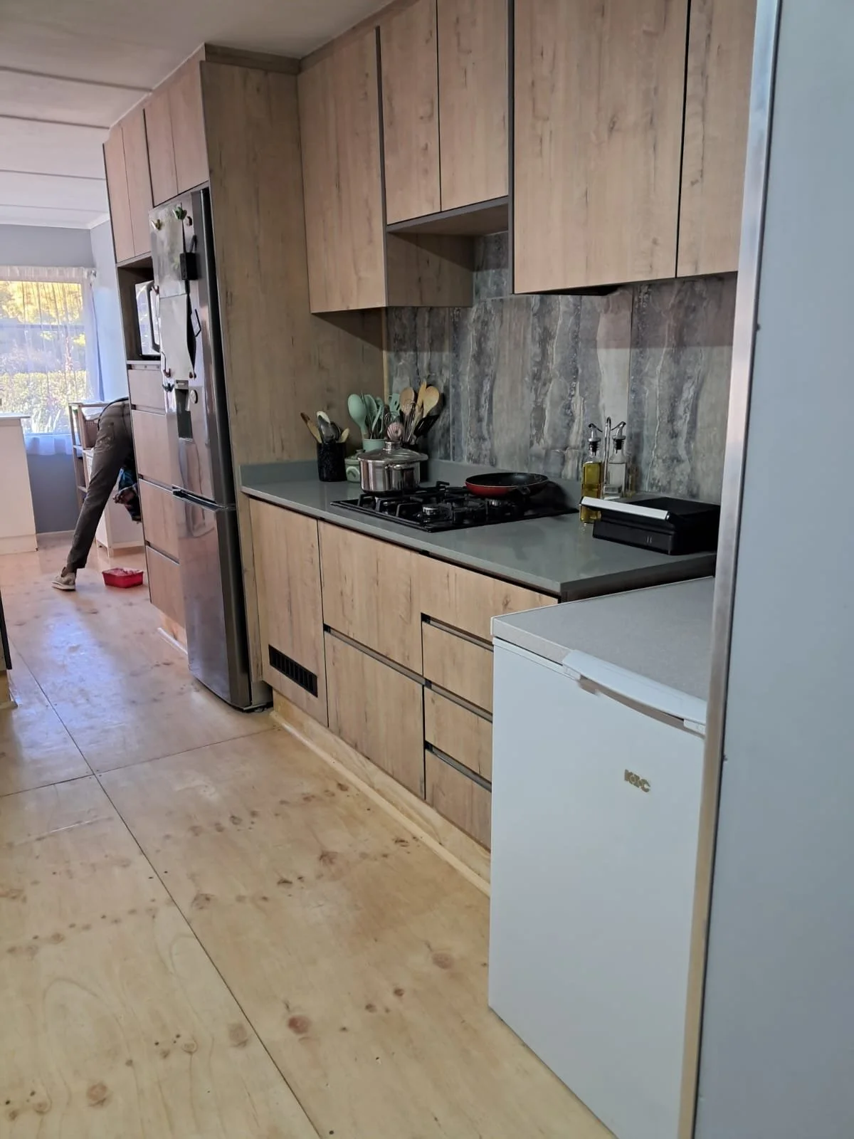Modern kitchen with light wood cabinets, a grey countertop, and a stone backsplash.