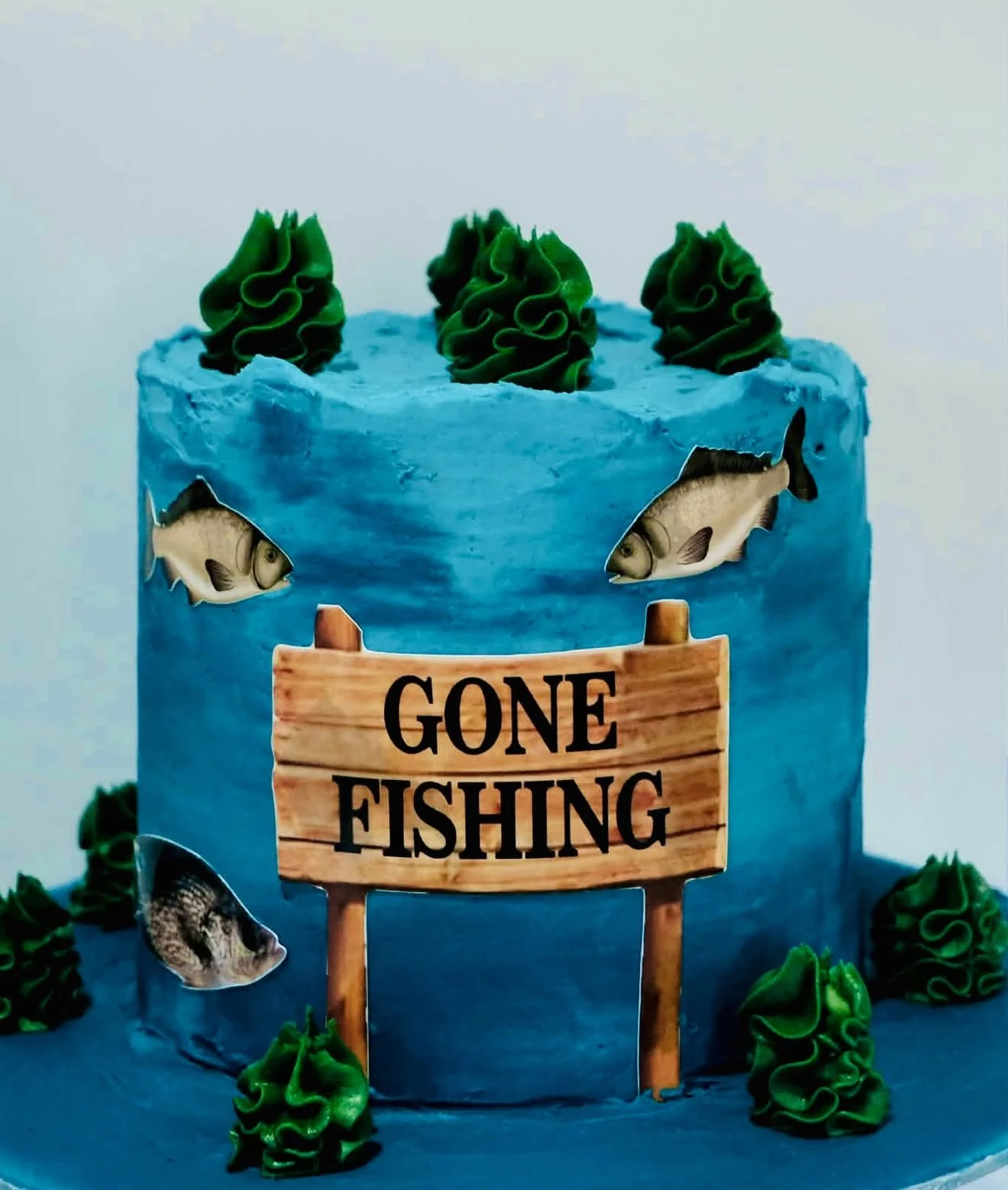 Blue cake decorated with fish images, green frosting swirls, and a sign that reads 'GONE FISHING'.
