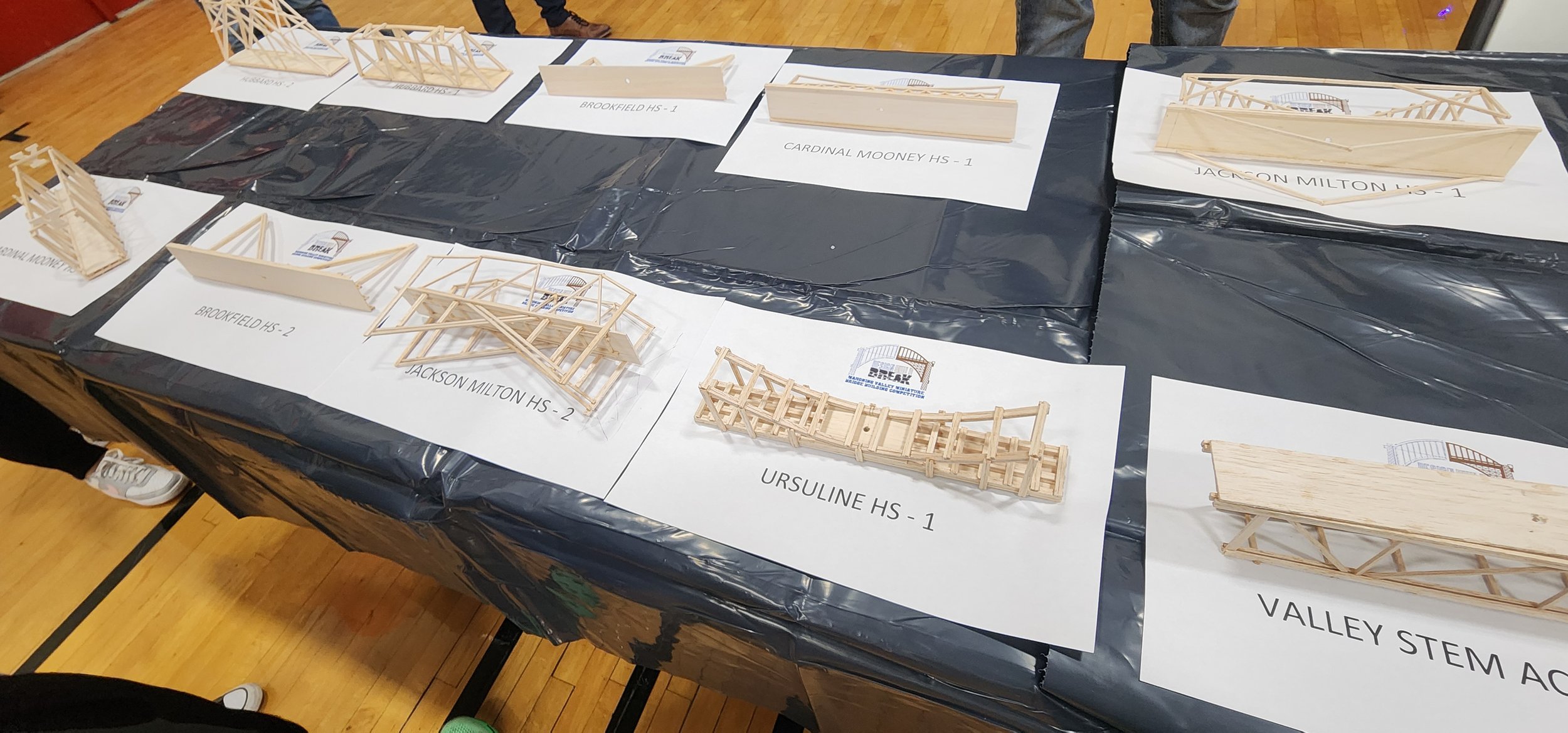 Wooden bridge models and bridges on a table with label cards from different high schools.