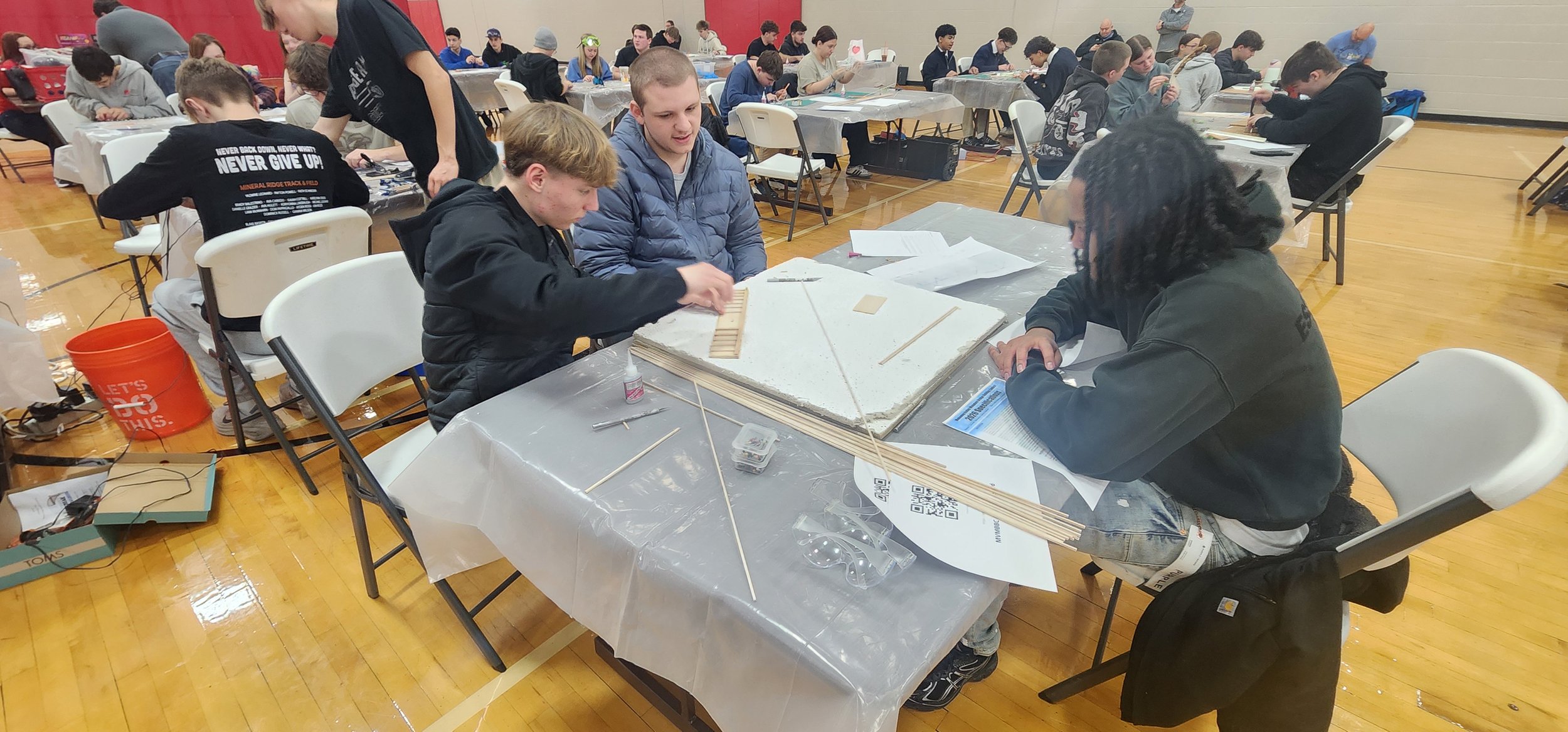Students working on a project at a table in a gymnasium during an event.
