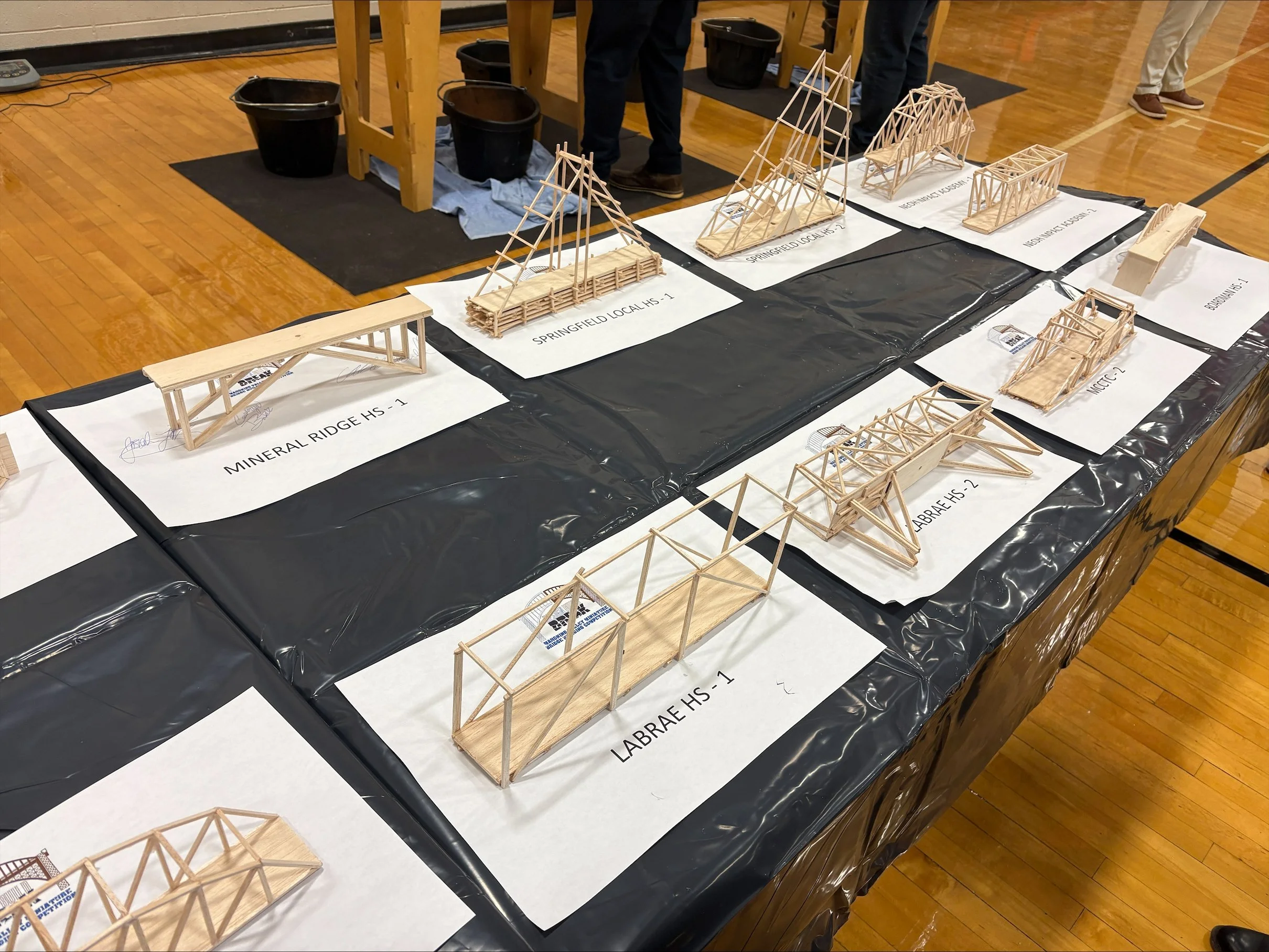 Various wooden architectural models displayed on a table with labels, in what appears to be a school or exhibition setting.