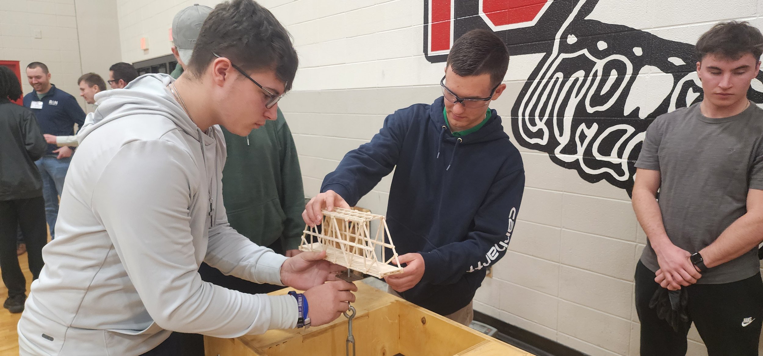 Group of young people examining a small wooden bridge model.