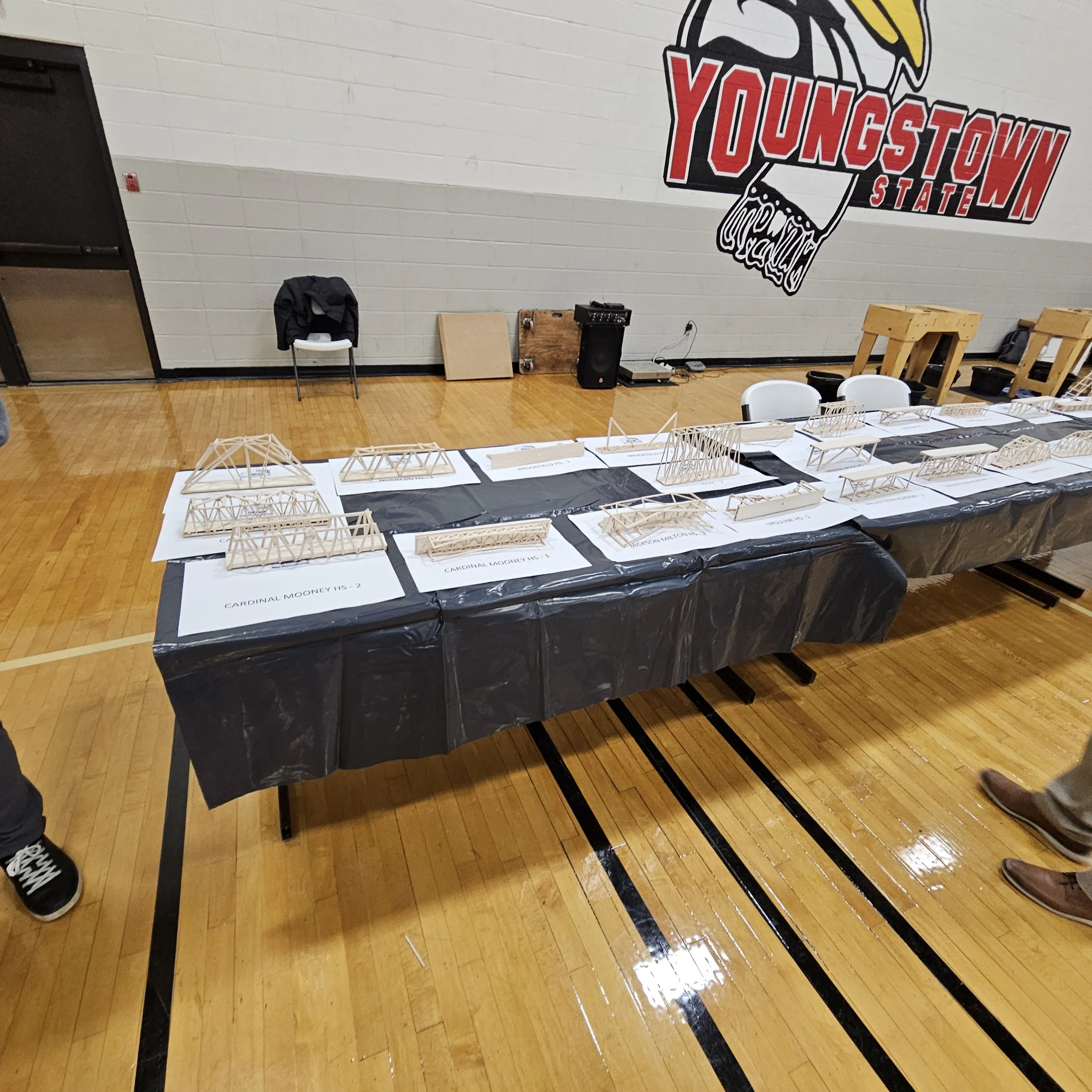 Display table with architectural models in a gymnasium, with a large mural of a football helmet and the words 'Youngstown State' on the wall.
