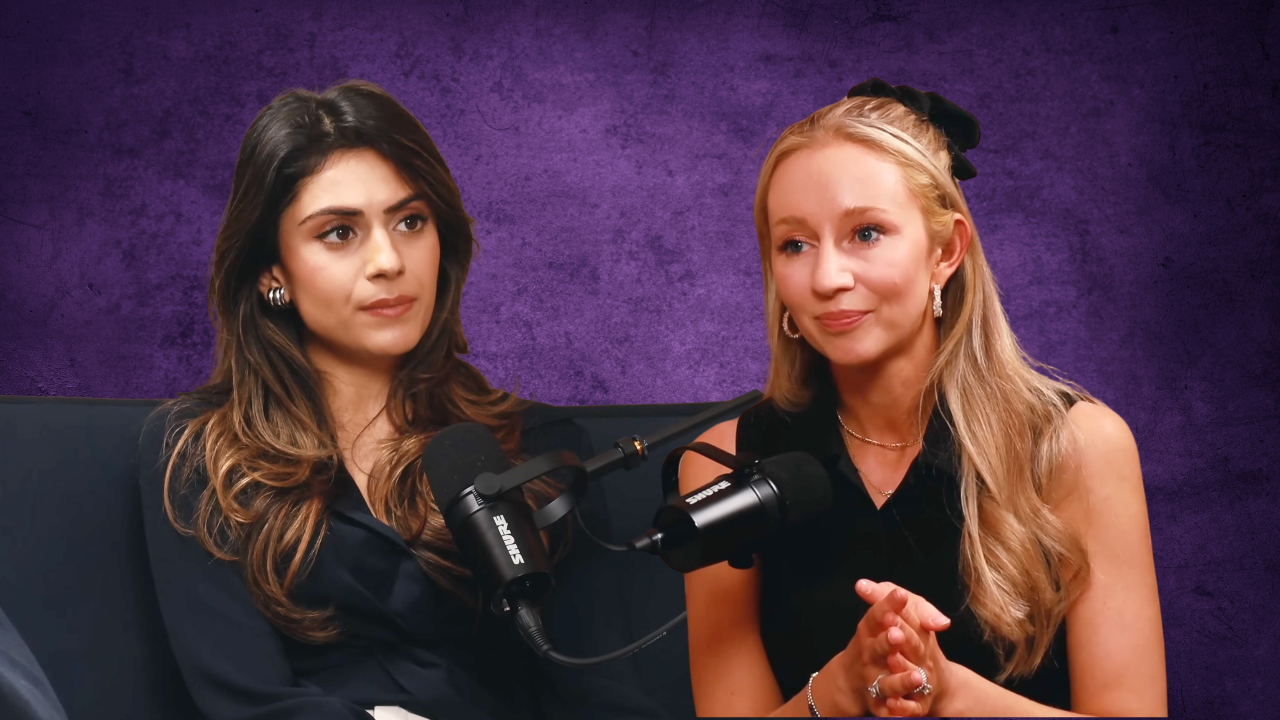 Two women sit in front of microphones during a podcast or interview, with a textured purple background behind them.