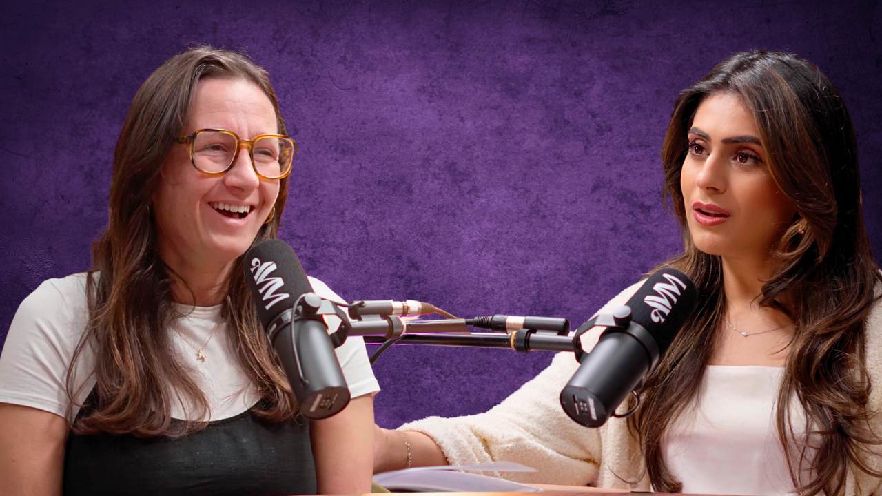 Two women recording a podcast or radio show with microphones in a studio with a purple backdrop.