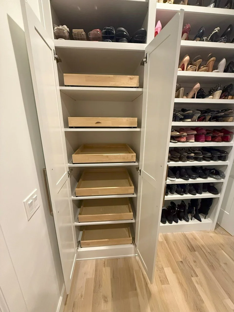 A closet with open double doors showing empty wooden shelves and shoe storage on the side.