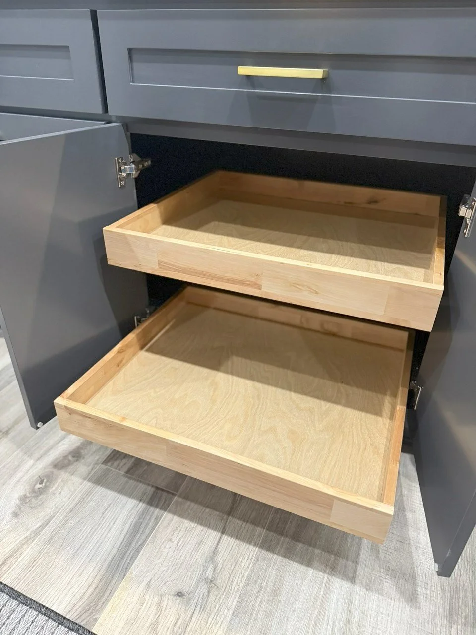 Open kitchen cabinet with two empty wooden drawers and dark gray doors.