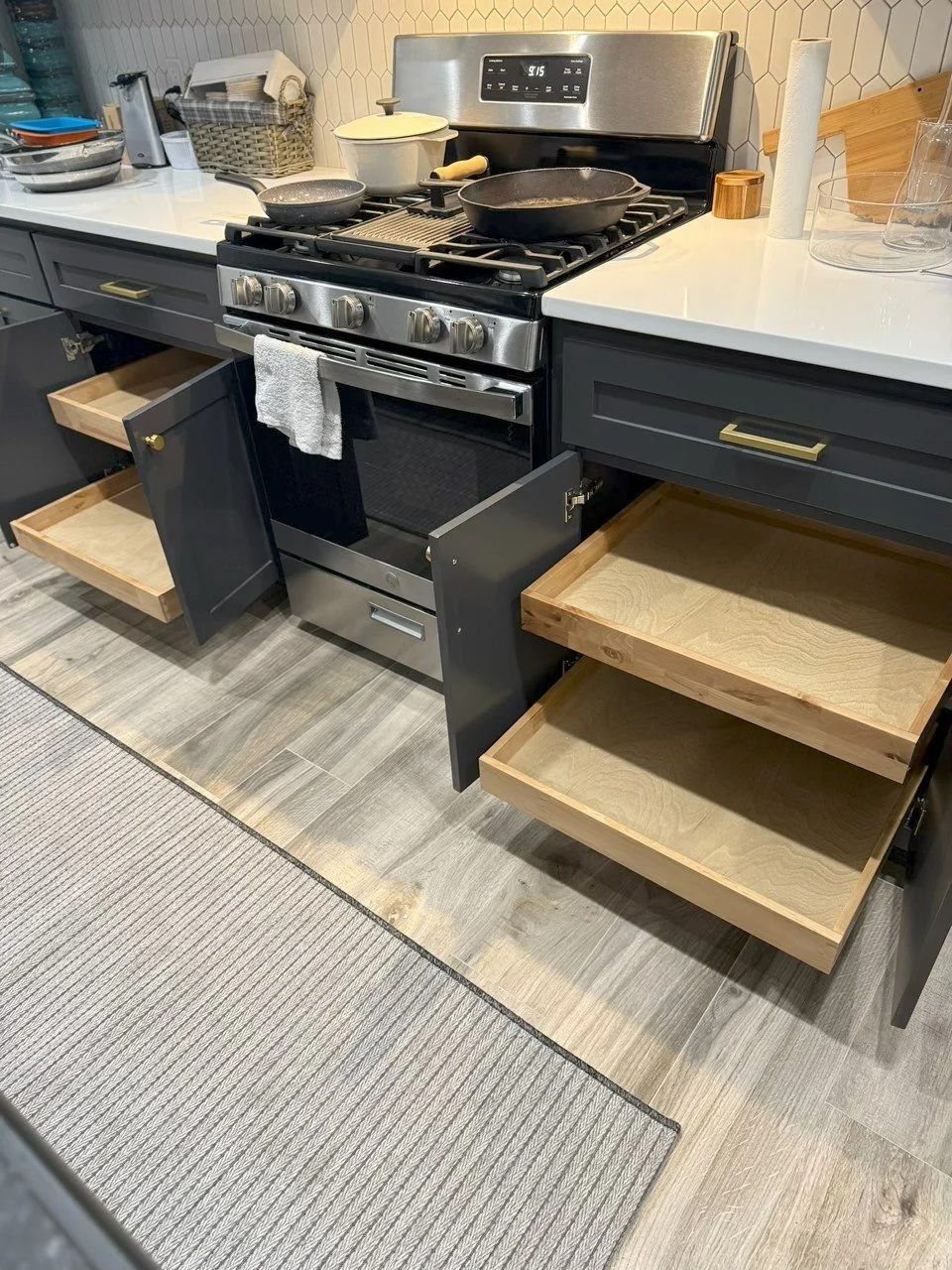 Open kitchen cabinets next to a stove with empty drawers and a towel hanging on the stove handle.