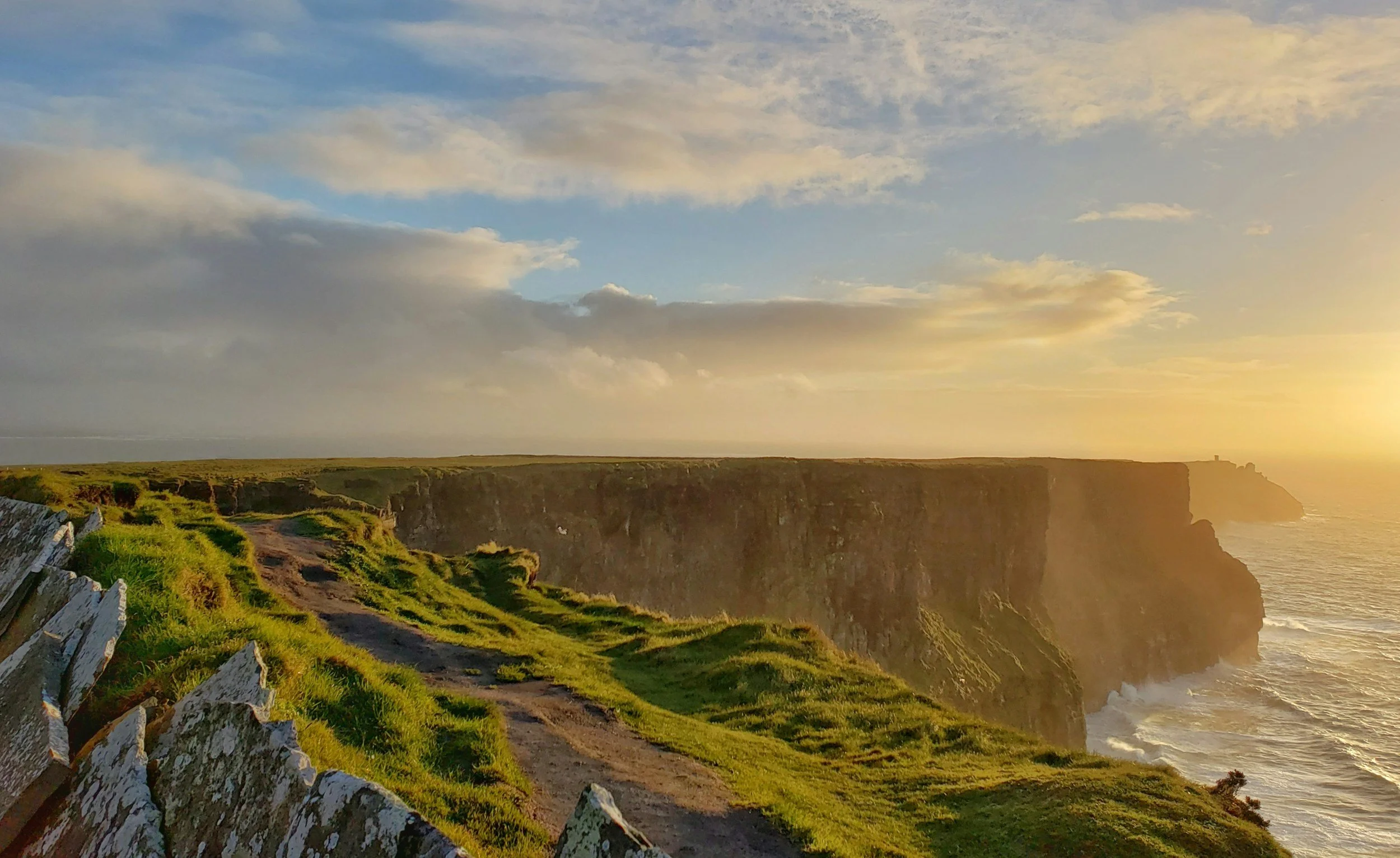 Cliffs overlooking the ocean during sunset with a path and white fence in the foreground.